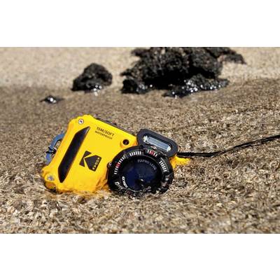 Eine gelbe Unterwasserkamera liegt teilweise im Wasser an einem sandigen Strand. Schwarze Felsen sind im Hintergrund sichtbar.