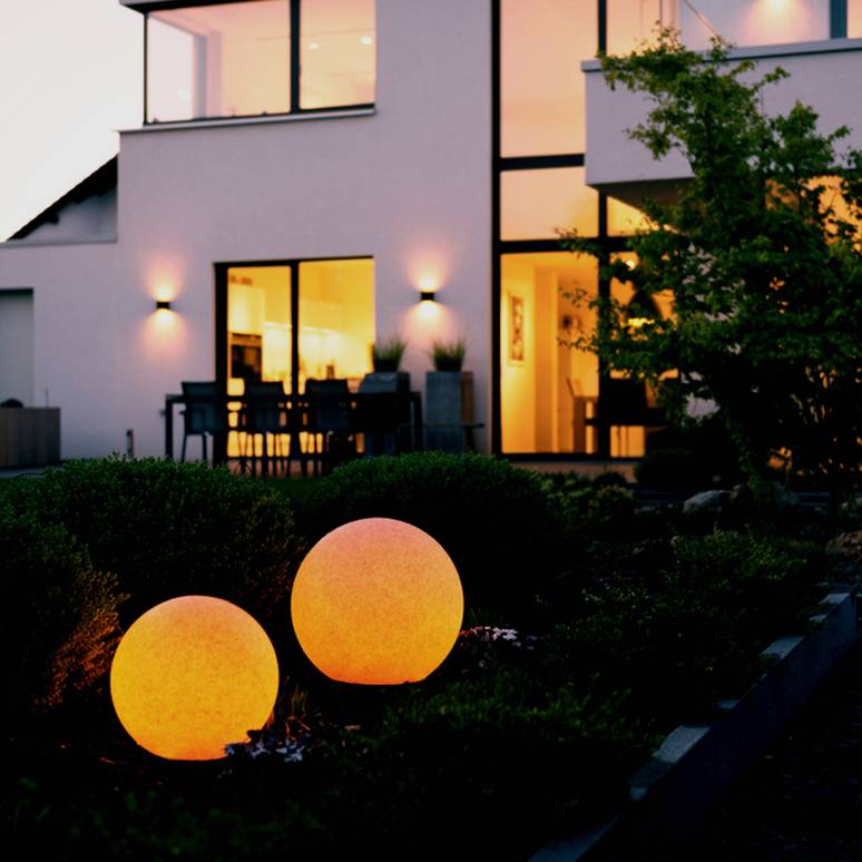 Ein modernes Haus bei Abenddämmerung mit großen, leuchtenden Kugeln im Garten, die eine warme Atmosphäre schaffen.