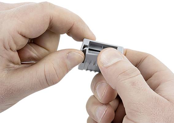 Hände halten einen grauen, rechteckigen Kunststoffstecker. Eine Hand steckt den Stecker zusammen, die andere hält ihn fest.