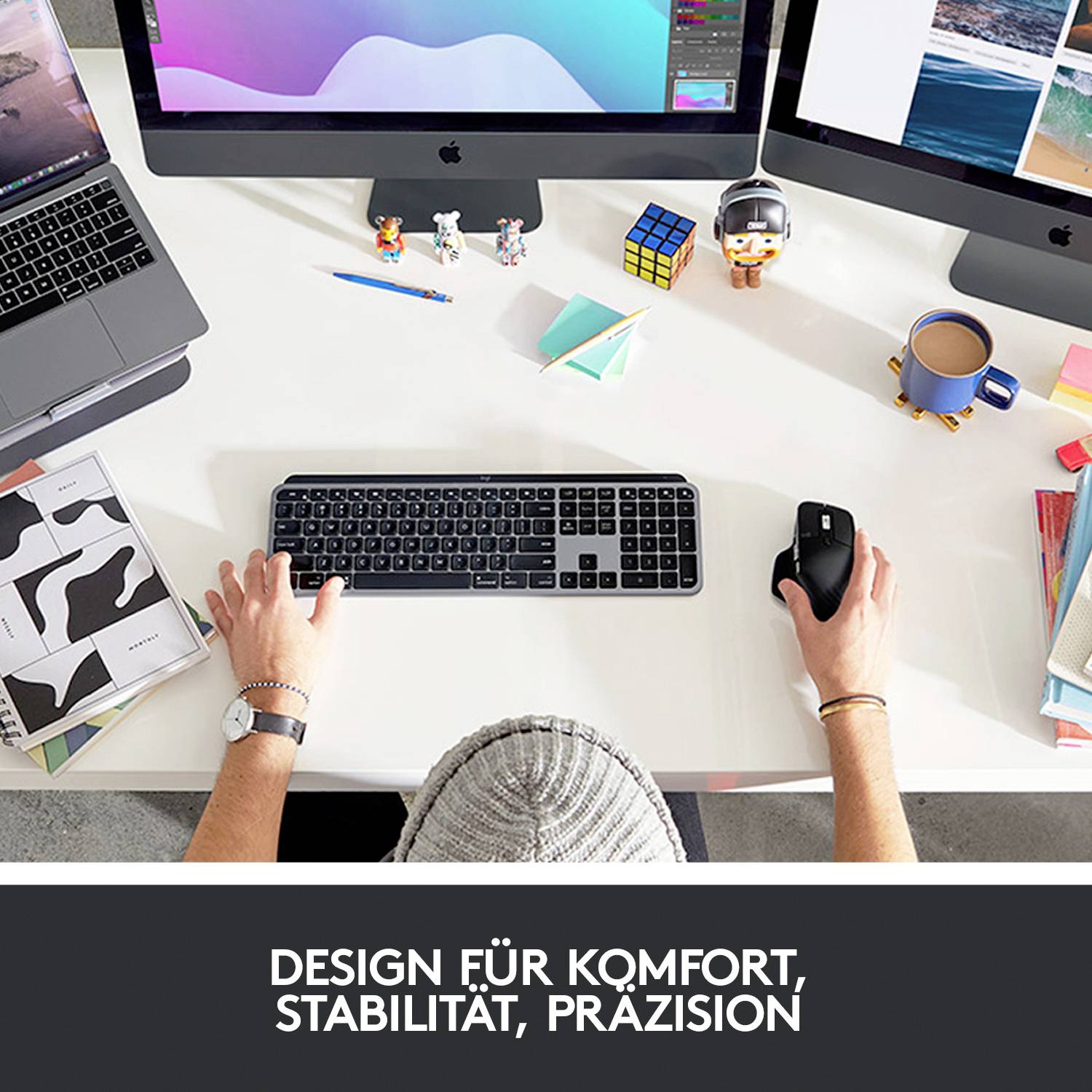 Arbeitsplatz von oben: Zwei Monitore, Laptop, Tastatur, Maus und Accessoires. Aufschrift unten: 'Design für Komfort, Stabilität, Präzision'.