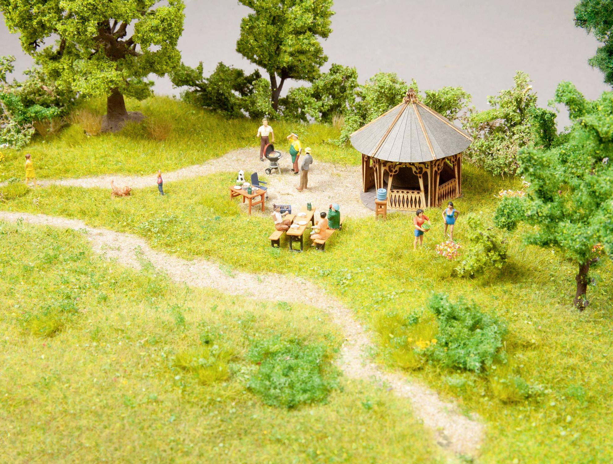 Ein Miniaturmodell zeigt einen Picknickplatz mit Pavillon, Tischen und Figuren beim Grillen in einer grünen Parklandschaft.
