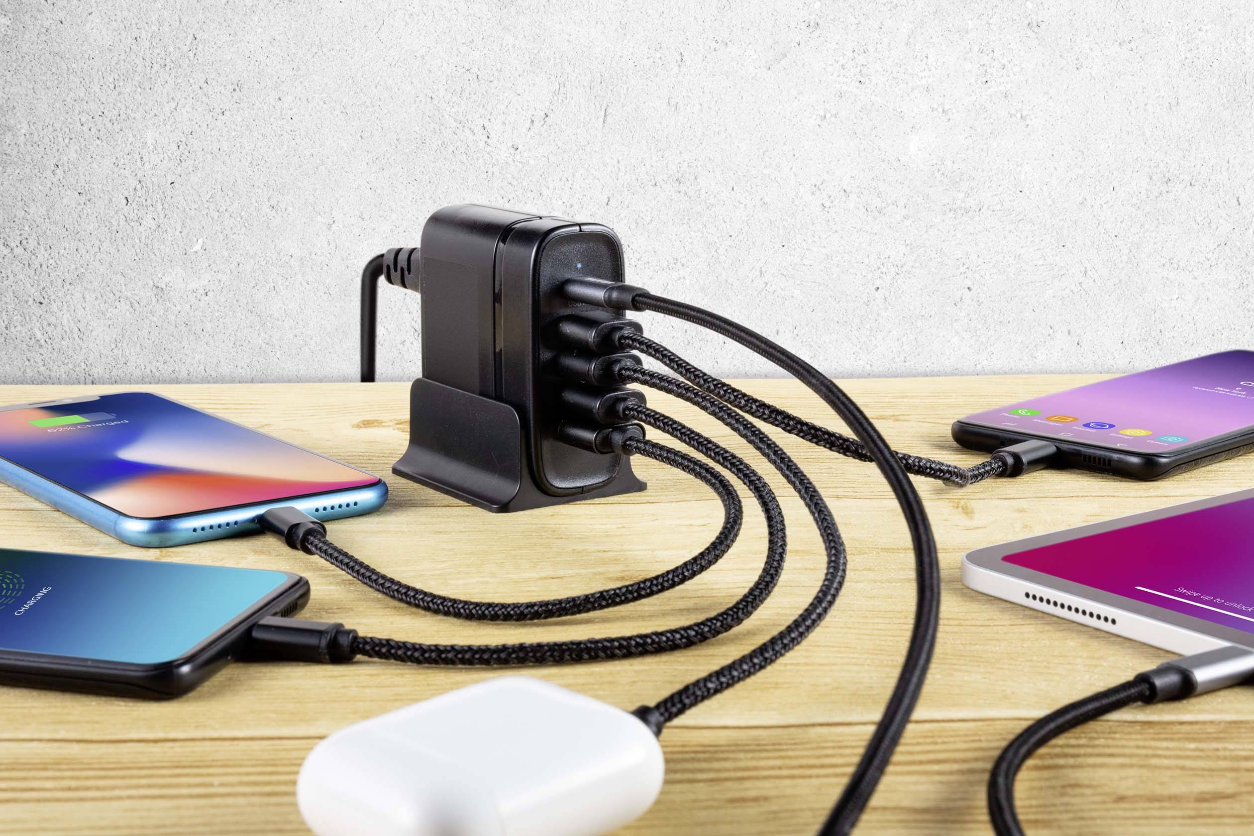 Mehrfach-USB-Ladegerät auf Holztisch lädt fünf Smartphones gleichzeitig. Kabel sind organisiert, Hintergrund ist unscharf.