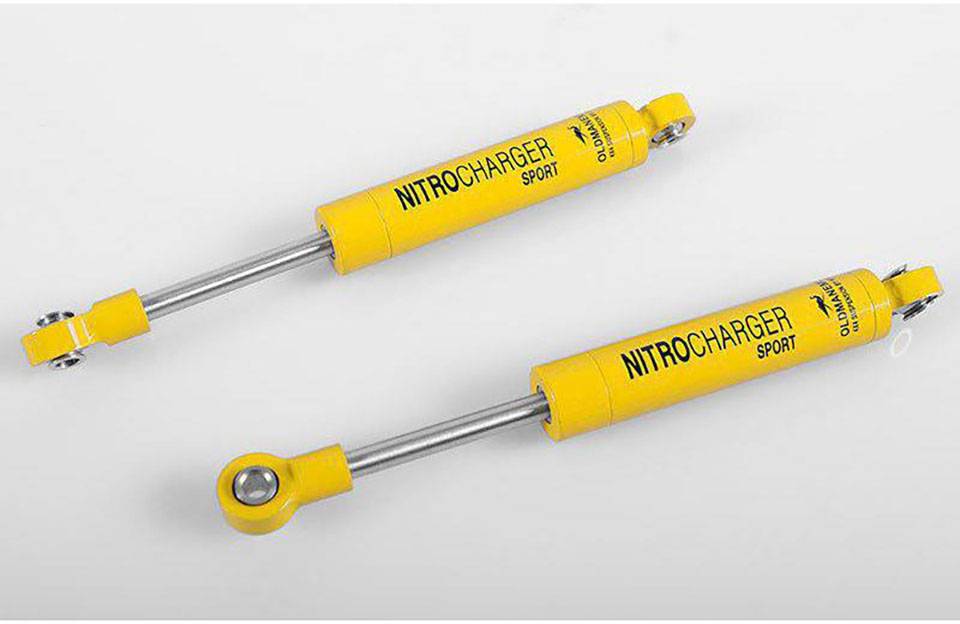 Zwei gelbe Stoßdämpfer mit der Aufschrift 'Nitrocharger Sport', auf grauem Hintergrund liegend.