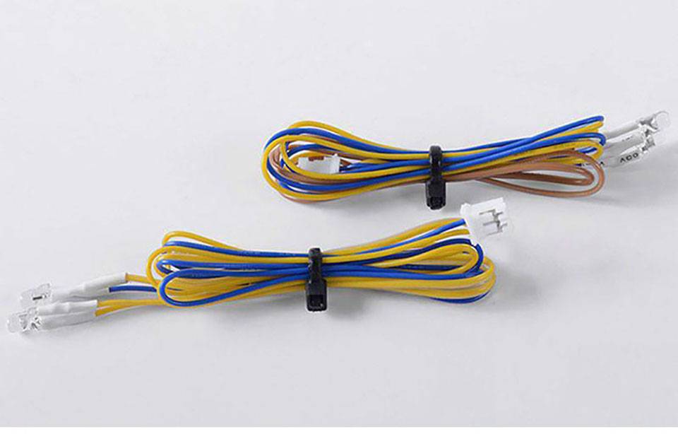Zwei Kabelbündel mit blauen, gelben und orangen Drähten, jeweils mit einem weißen Stecker, liegen nebeneinander auf einer Fläche.