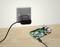Ein Raspberry Pi ist auf einem Holztisch zu sehen, verbunden mit einem Netzteil, das in einer Steckdose steckt.