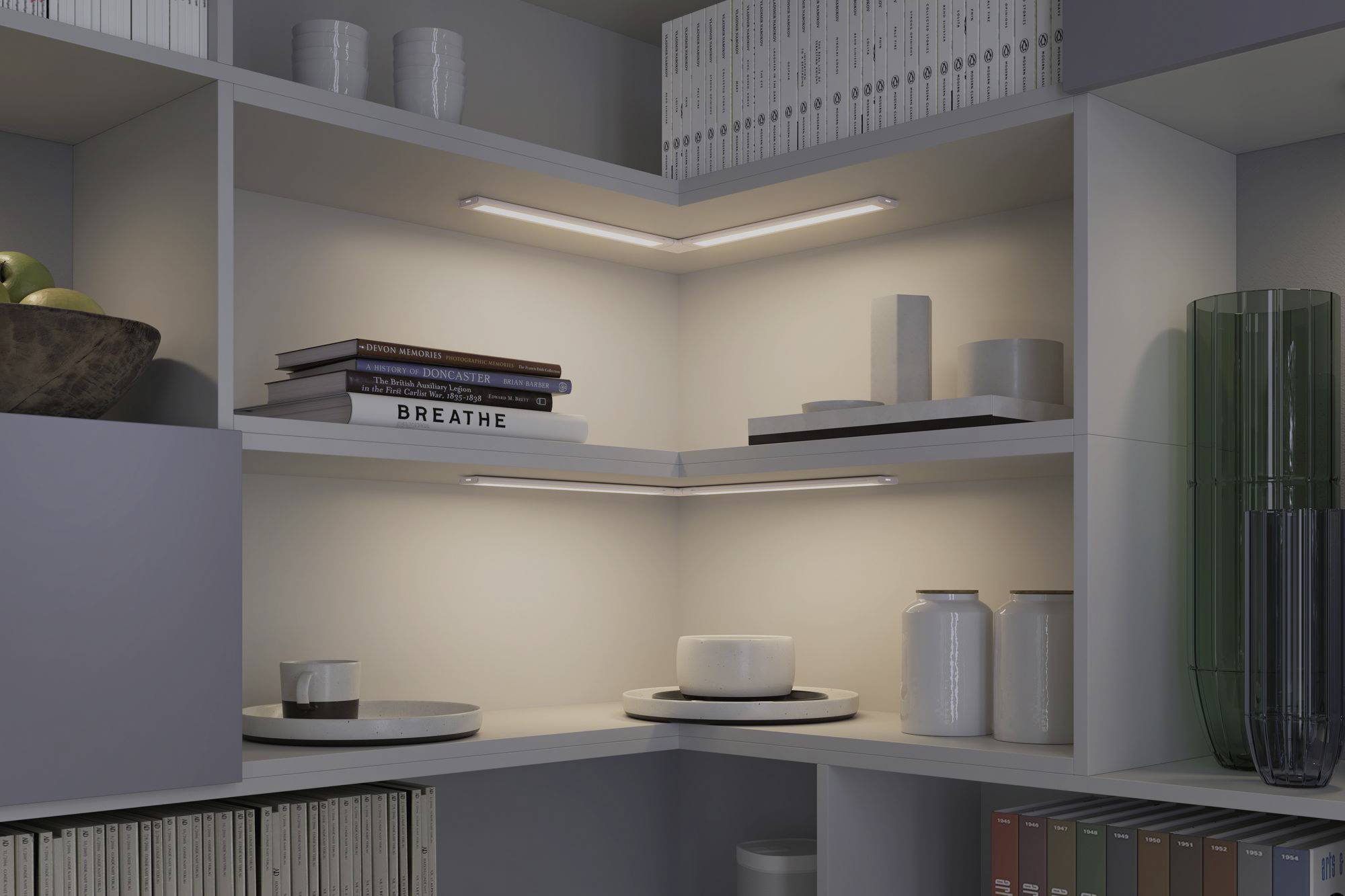 Ein modernes Regal mit minimalistischem Design. Bücher, eine Obstschale und dekorative Gegenstände sind ordentlich arrangiert. Beleuchtung schafft eine gemütliche Atmosphäre.