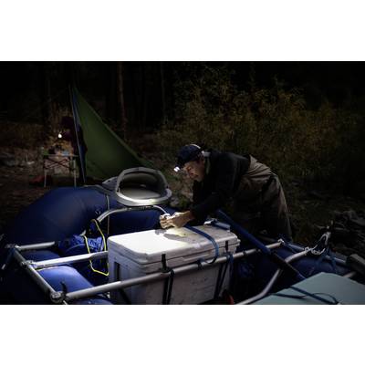 Eine Person mit Stirnlampe arbeitet nachts an einem aufblasbaren Boot mit Ausrüstung darauf. Im Hintergrund ist ein Zelt erkennbar.
