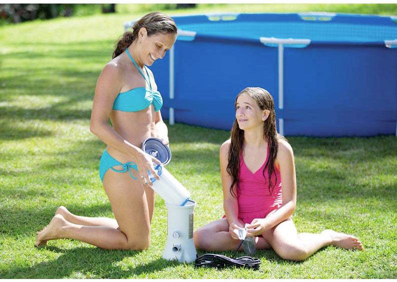 Zwei Personen im Badeanzug neben einem Pool im Freien, die eine Poolpumpe überprüfen. Eine Person hält einen Filter, die andere einen Schlauch.