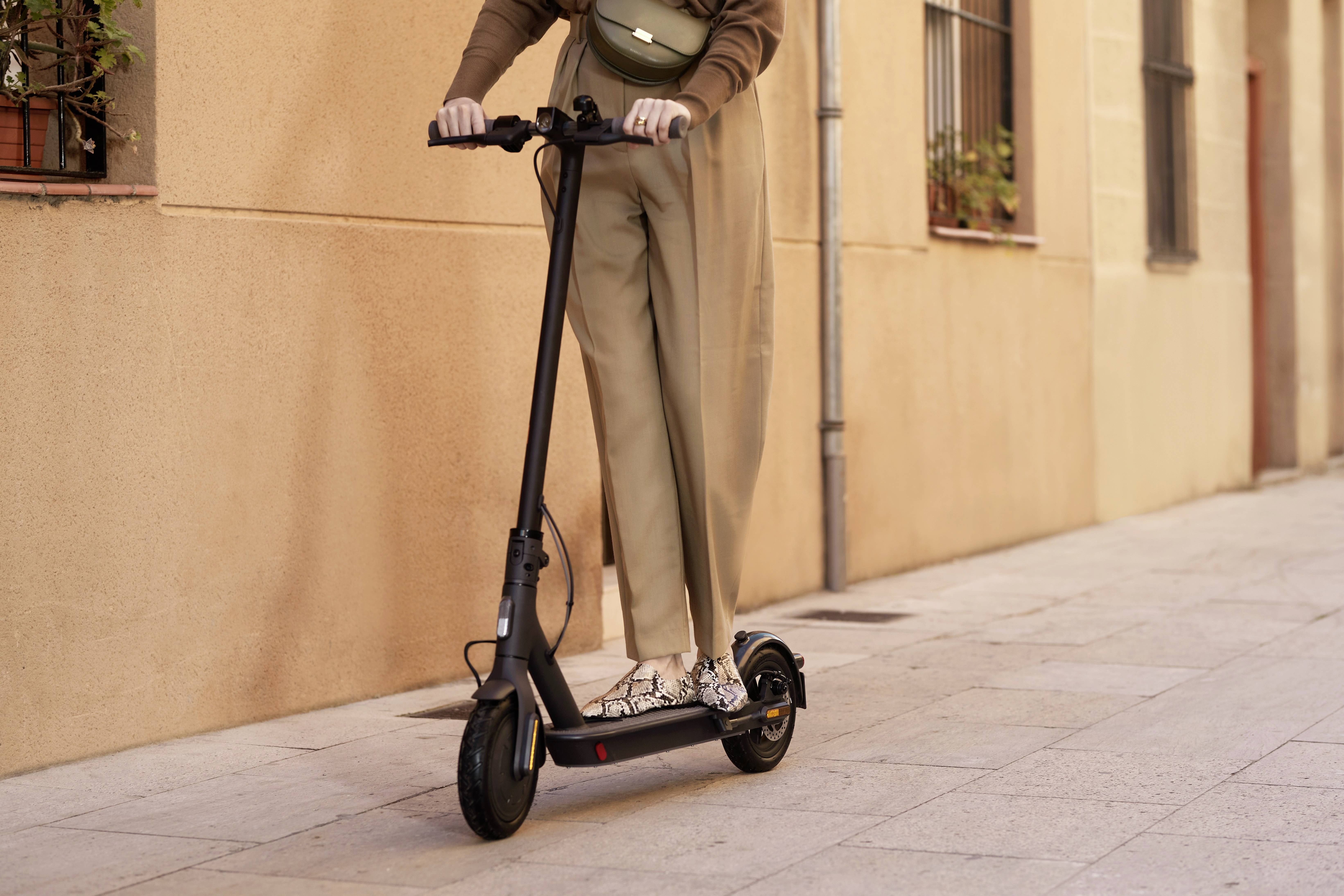 Person fährt auf einem schwarzen Elektroroller eine gepflasterte Straße entlang; Stadtumgebung mit beige Gebäude im Hintergrund.