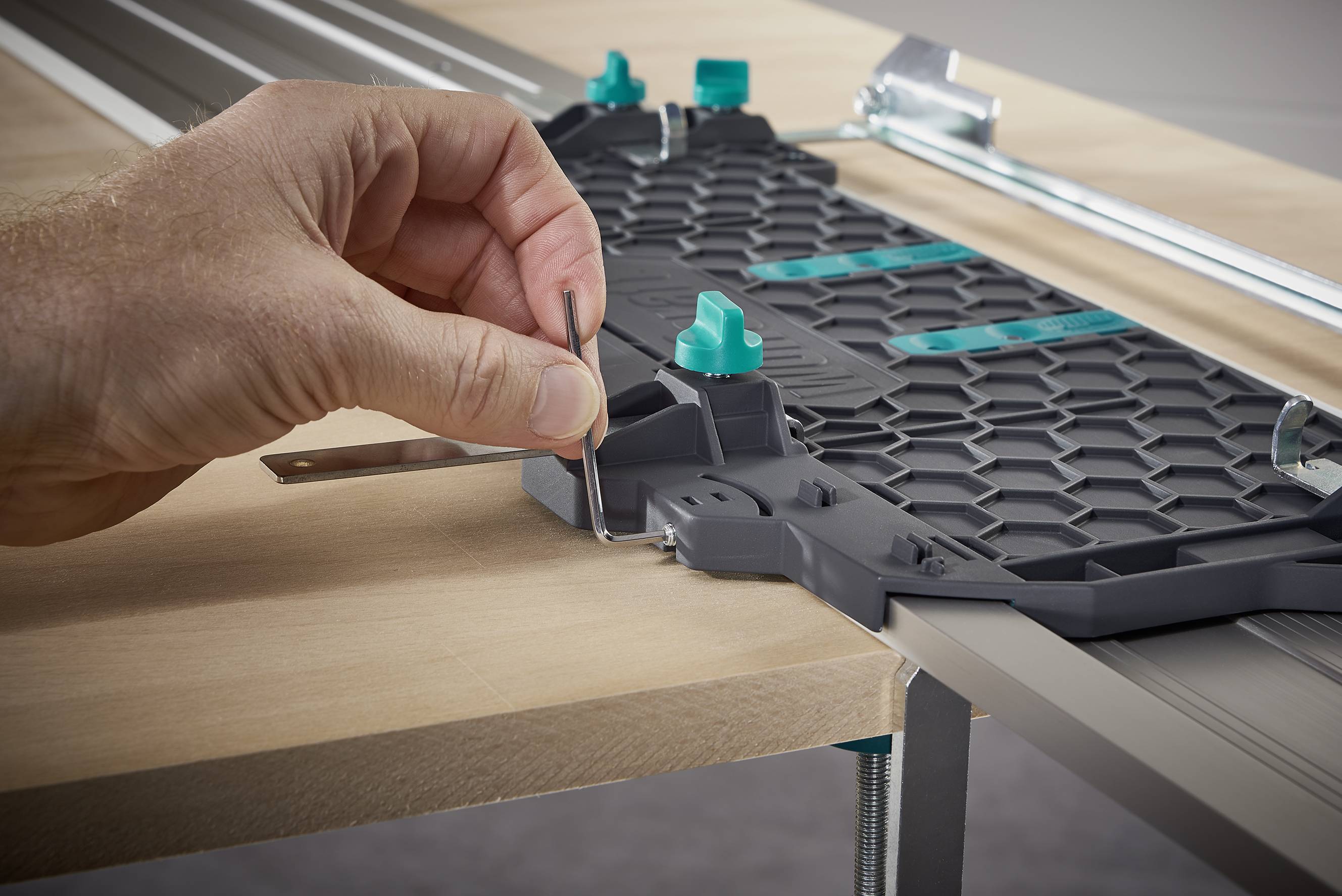 Eine Hand positioniert eine Metallklammer auf einem Tisch, die als Teil eines Werkzeugsystems zur Holzfaserführung verwendet wird.