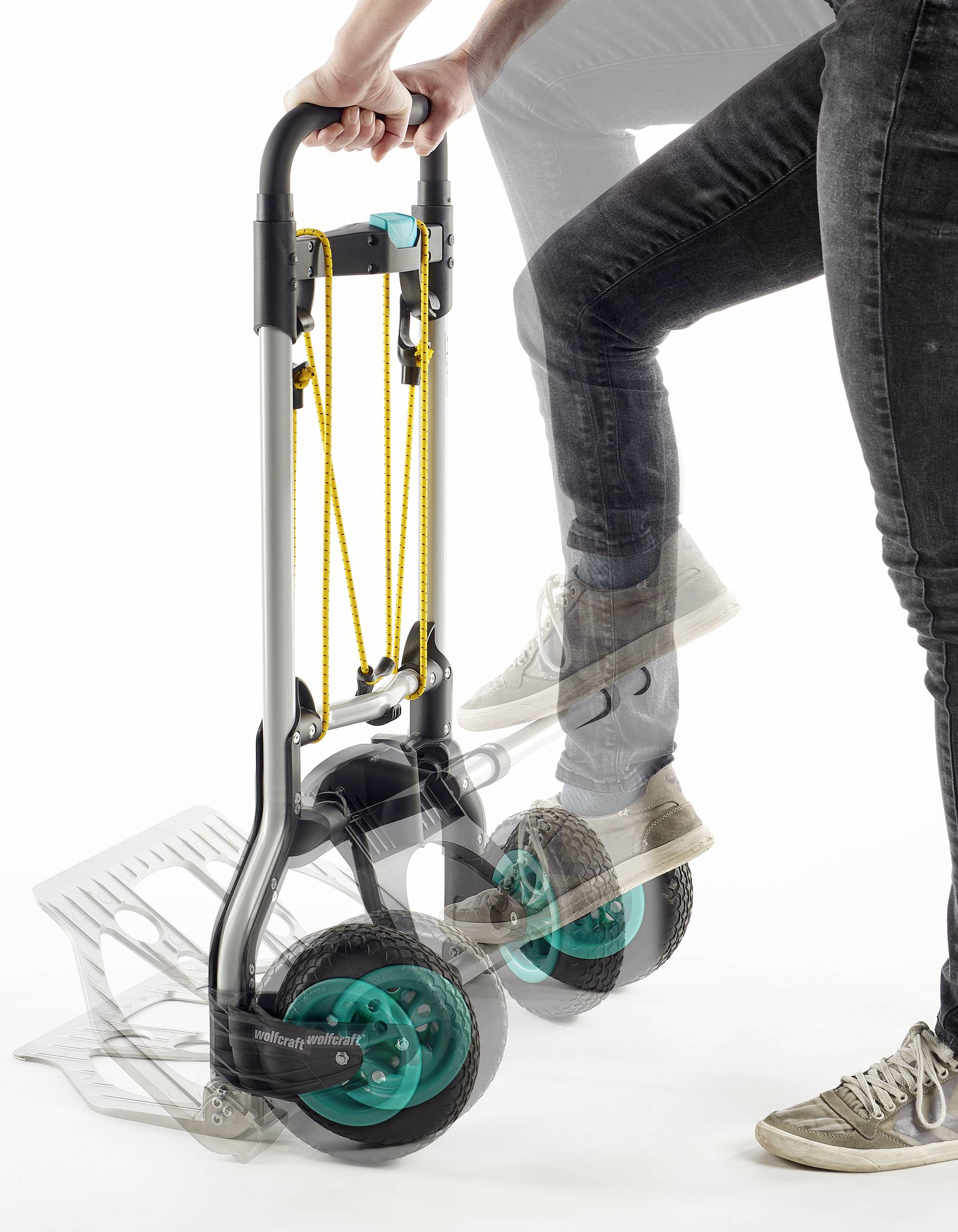 Eine Handkarre mit großen, grünen Rädern wird verwendet. Eine Person bewegt sie über eine Treppe.