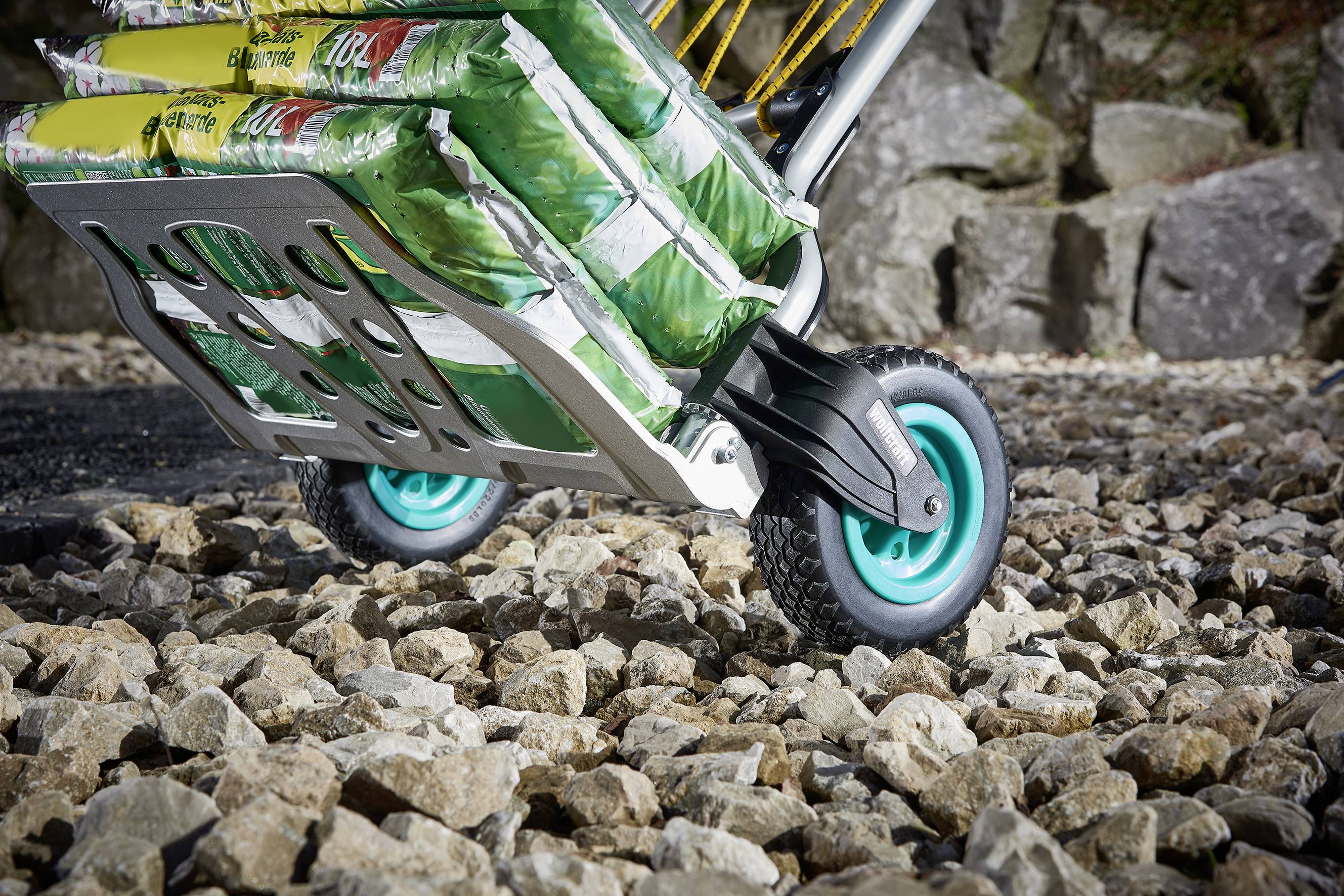 Eine Schubkarre mit zwei vorderen Rädern transportiert mehrere Säcke auf einem felsigen Untergrund.