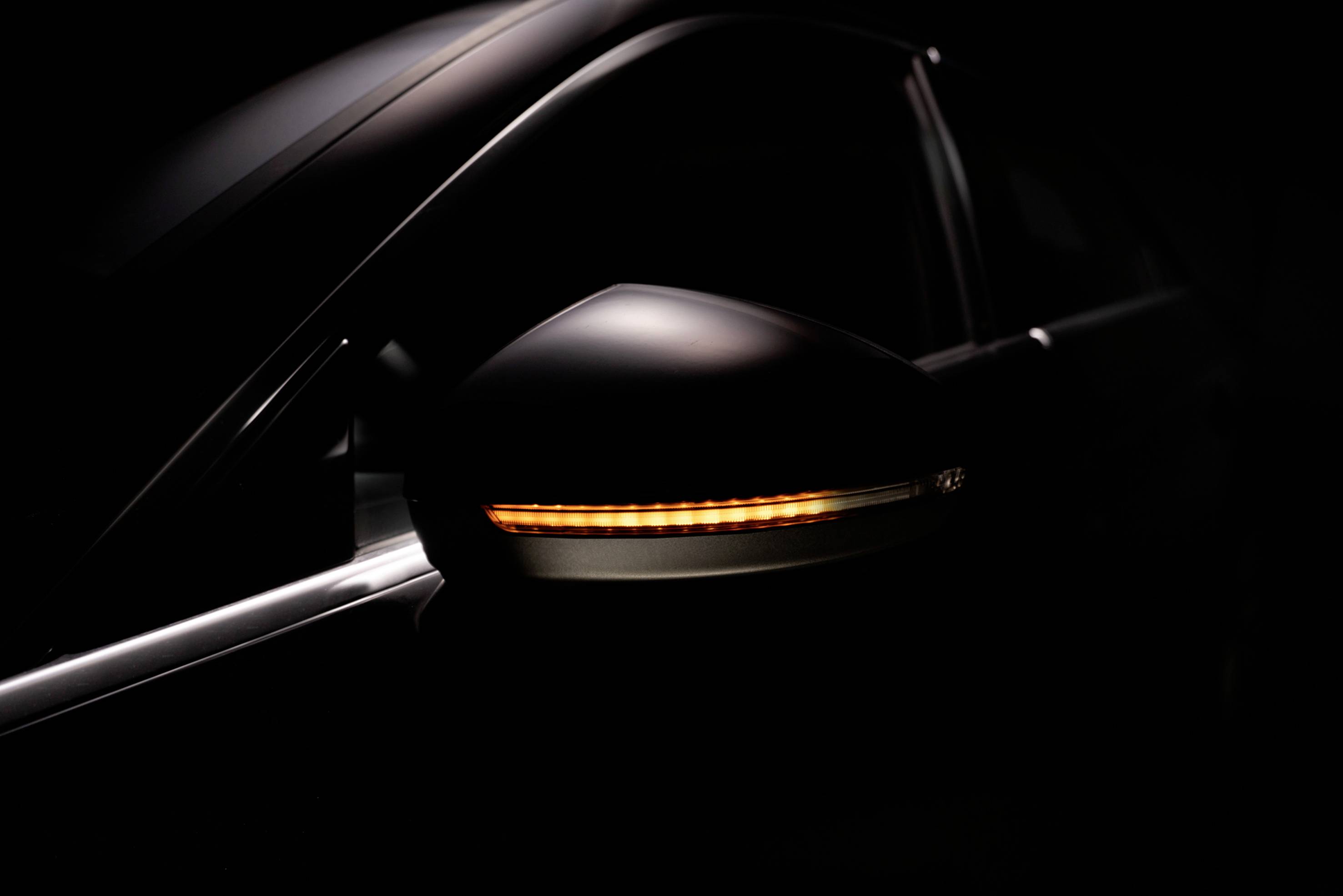 Nahaufnahme eines Seitenblinkers eines Autos, der orange leuchtet, auf dunklem Hintergrund.