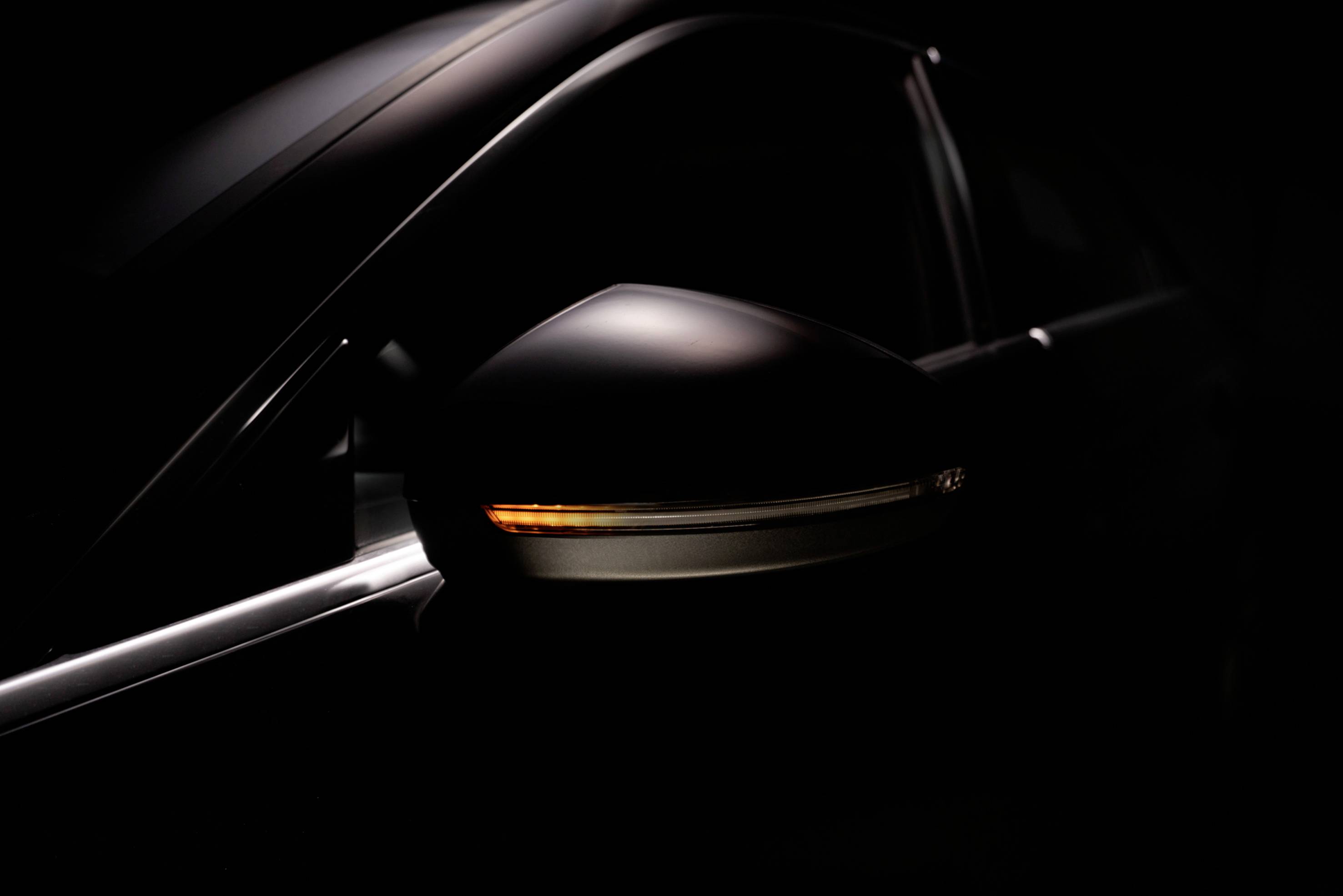 Ein Seitenspiegel eines Autos mit eingeschaltetem Blinker bei schwachem Licht, was die elegante Form des Fahrzeugs hervorhebt.