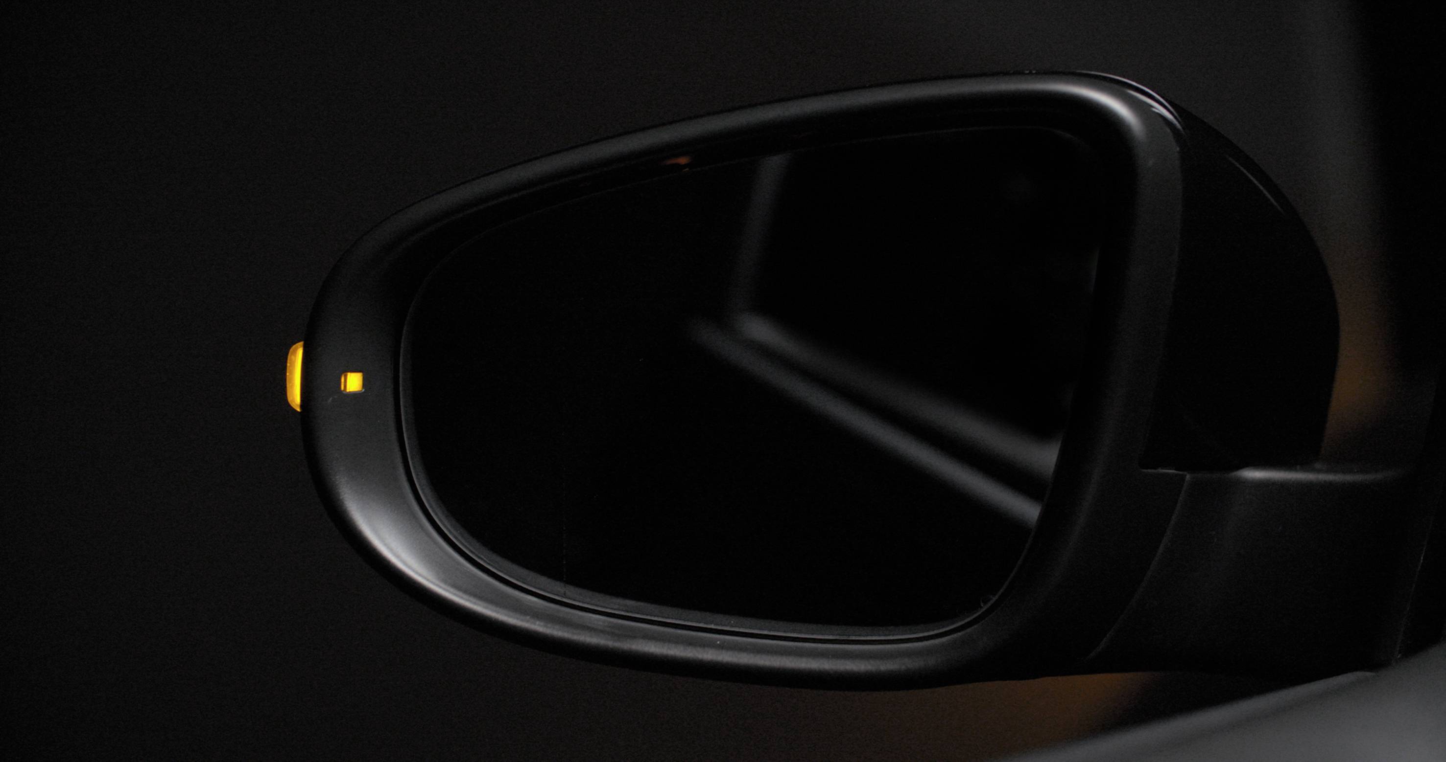 Seitenspiegel eines Autos mit leuchtendem Warnsymbol, das einen toten Winkel oder ein nahendes Fahrzeug anzeigt.