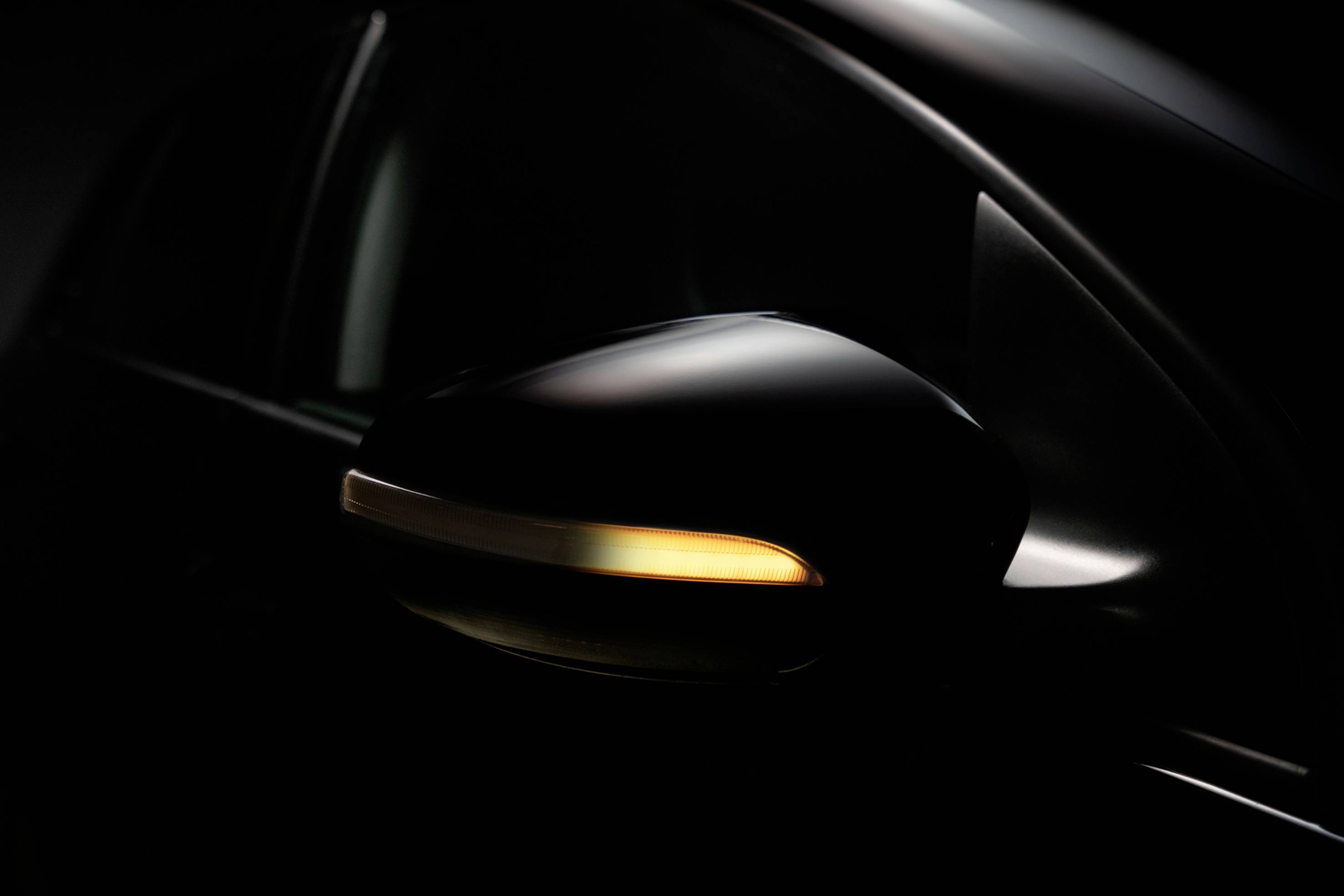 Ein Auto-Außenspiegel mit eingeschaltetem Blinker in dunkler Umgebung.