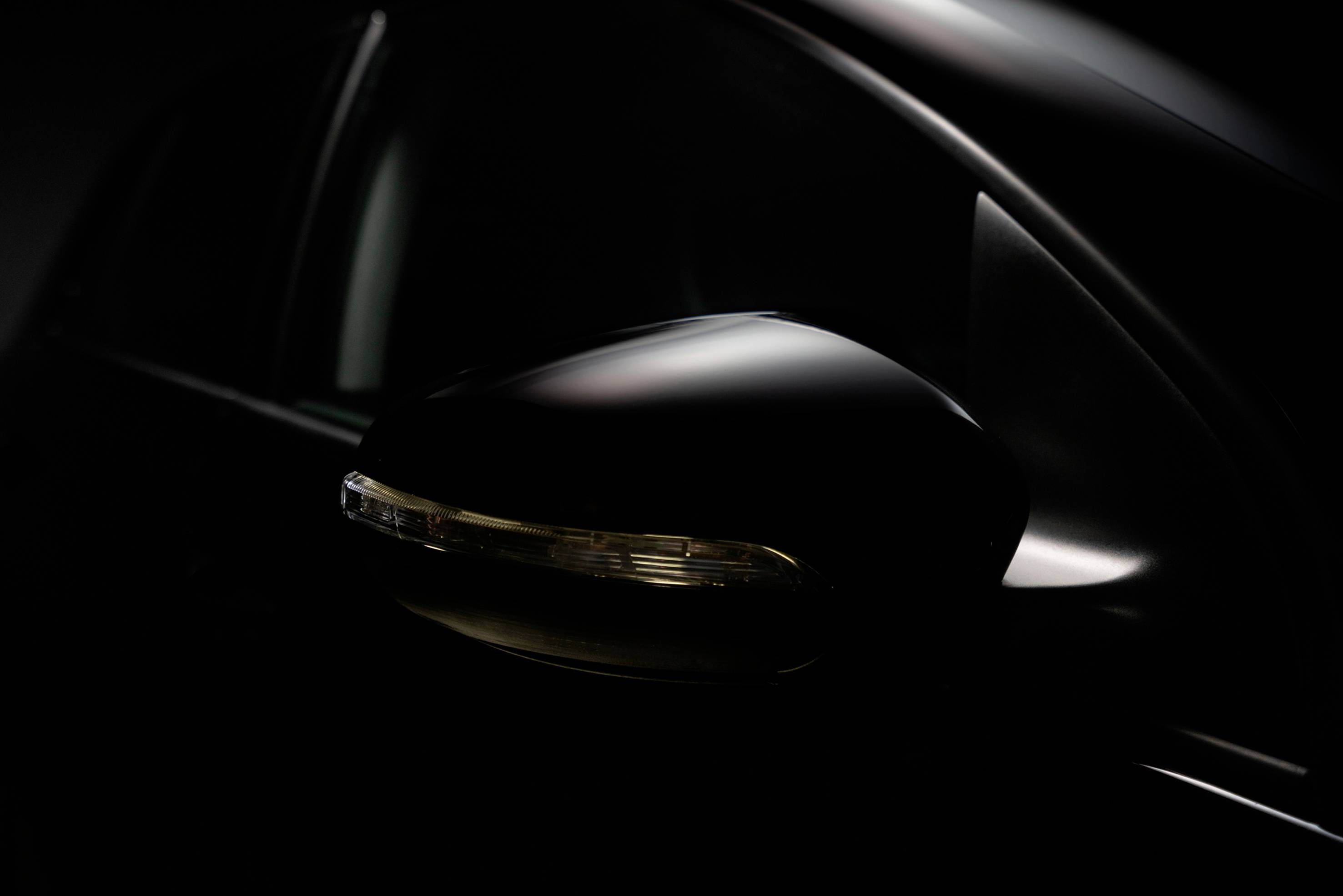 Ein seitlicher Rückspiegel eines schwarzen Autos im Dunkeln, der elegant beleuchtet wird und eine moderne, aerodynamische Form zeigt.
