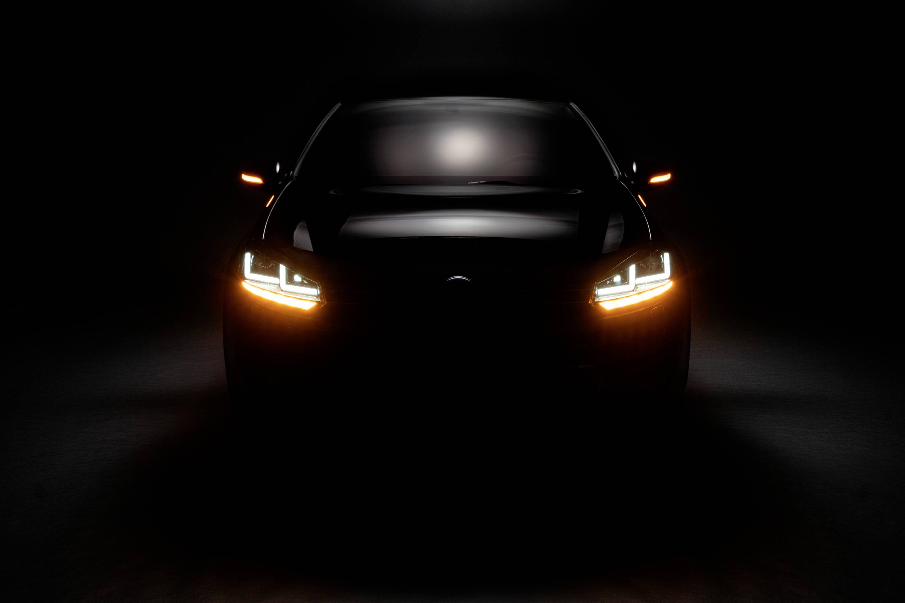 Dunkles Auto mit eingeschalteten Frontlichtern, betont durch stimmungsvolle Beleuchtung, frontal von vorne fotografiert.