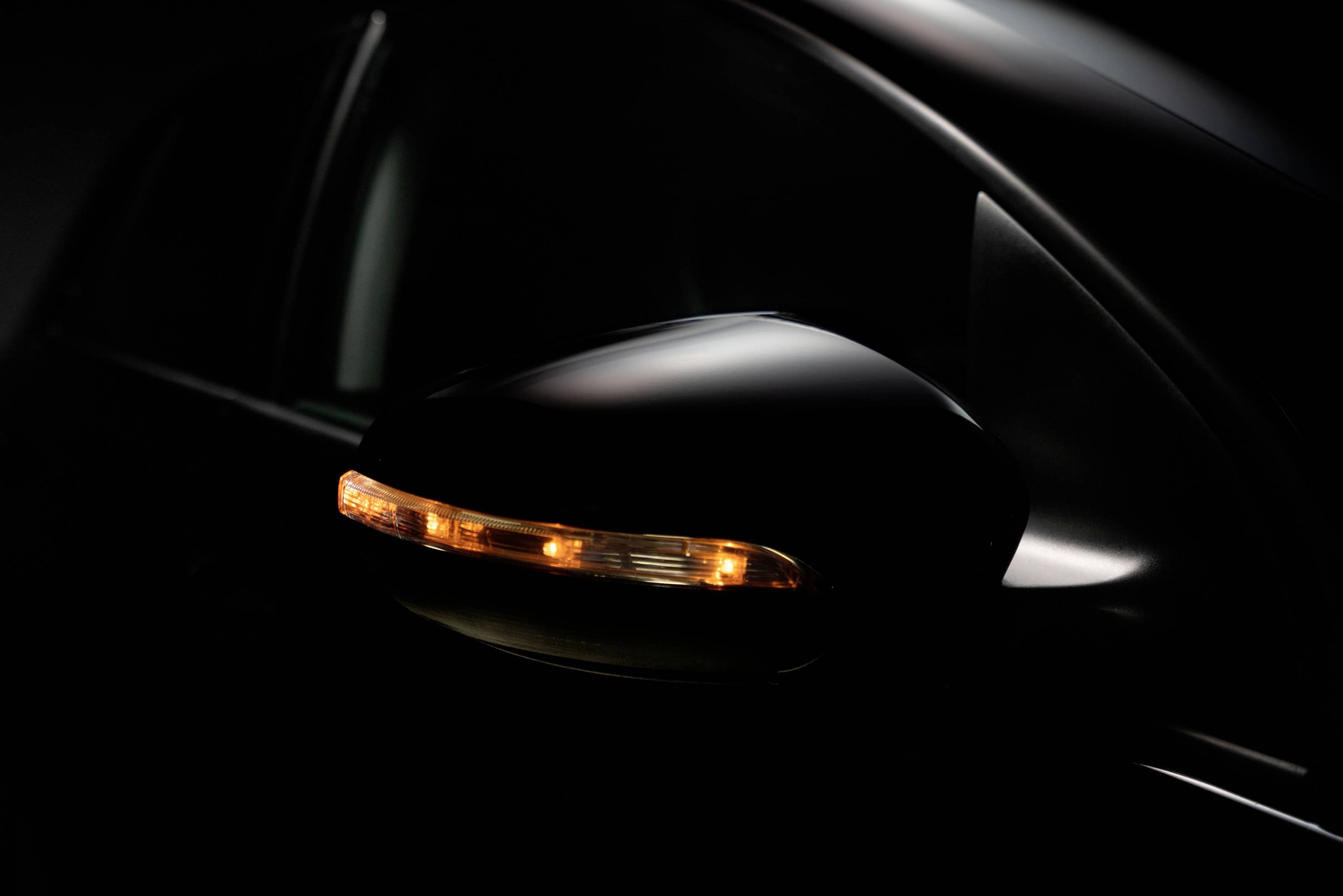 Ein Auto-Seitenspiegel mit eingeschaltetem Blinker bei Dunkelheit; der orangefarbene Lichtstreifen hebt sich vom schwarzen Hintergrund ab.
