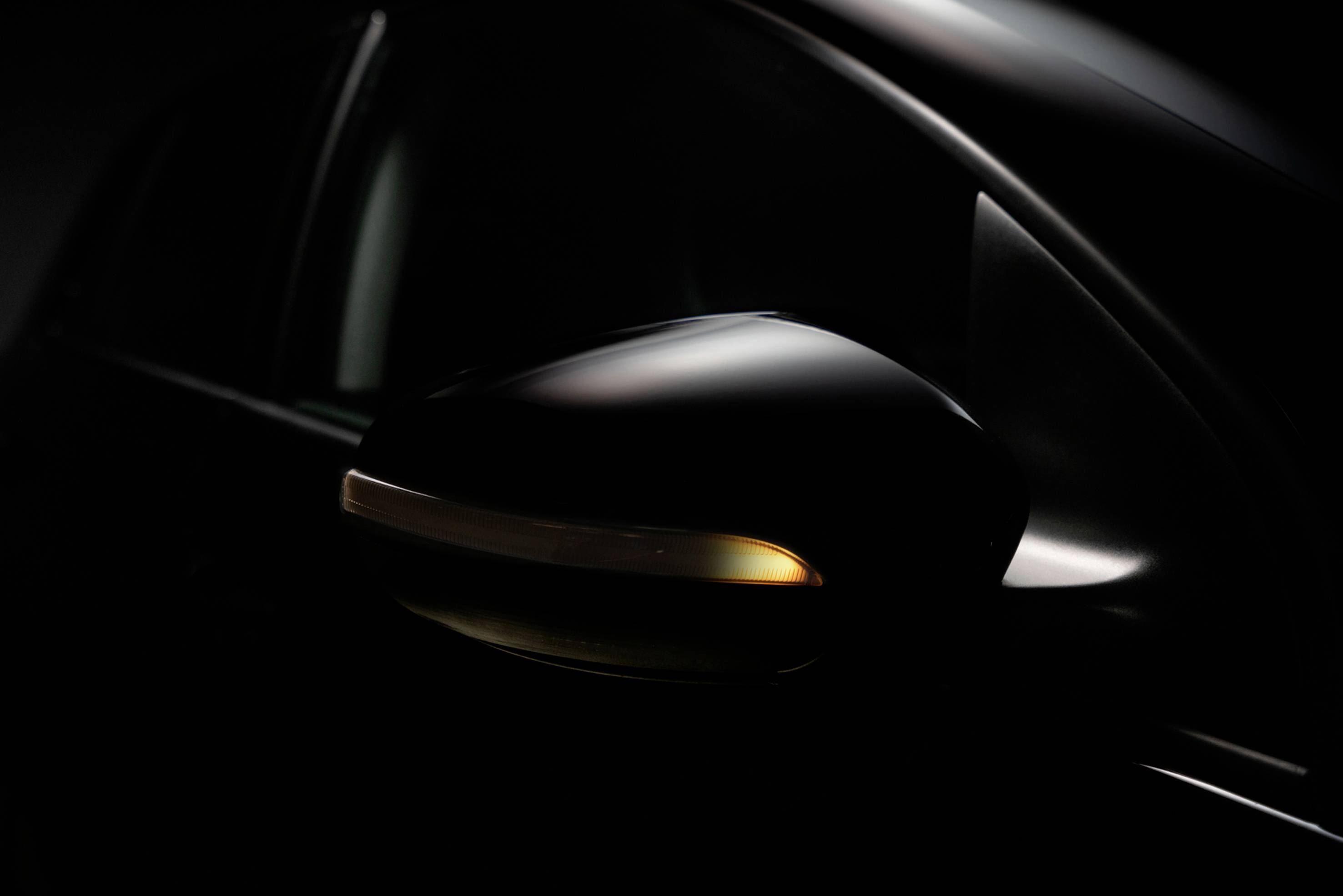 Schwarzer Autospiegel mit eingeschaltetem Blinkerlicht, nahansicht.