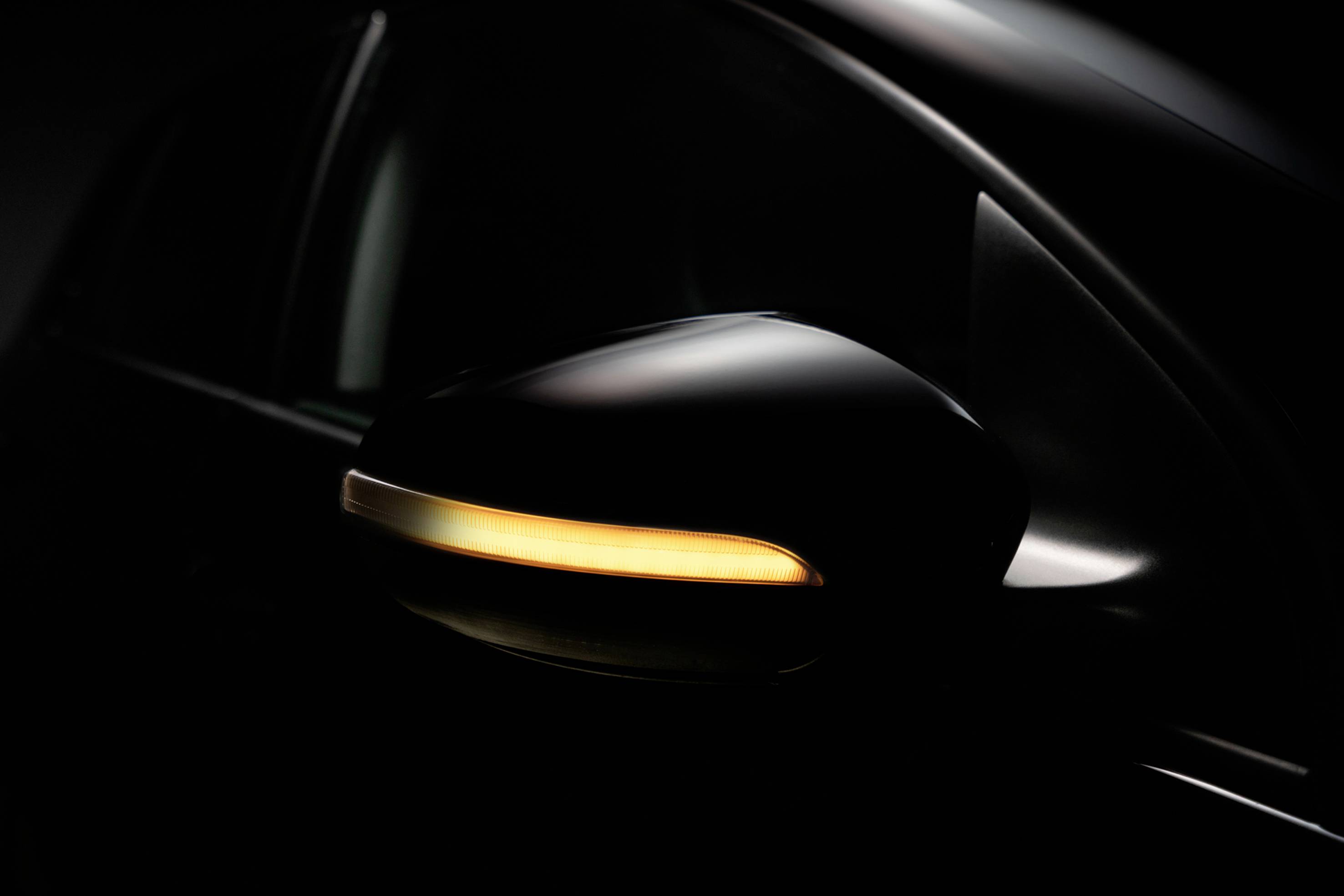 Ein Seitenrückspiegel eines Autos mit eingeschaltetem, gelbem Blinker, dargestellt in einem dunklen Umfeld.