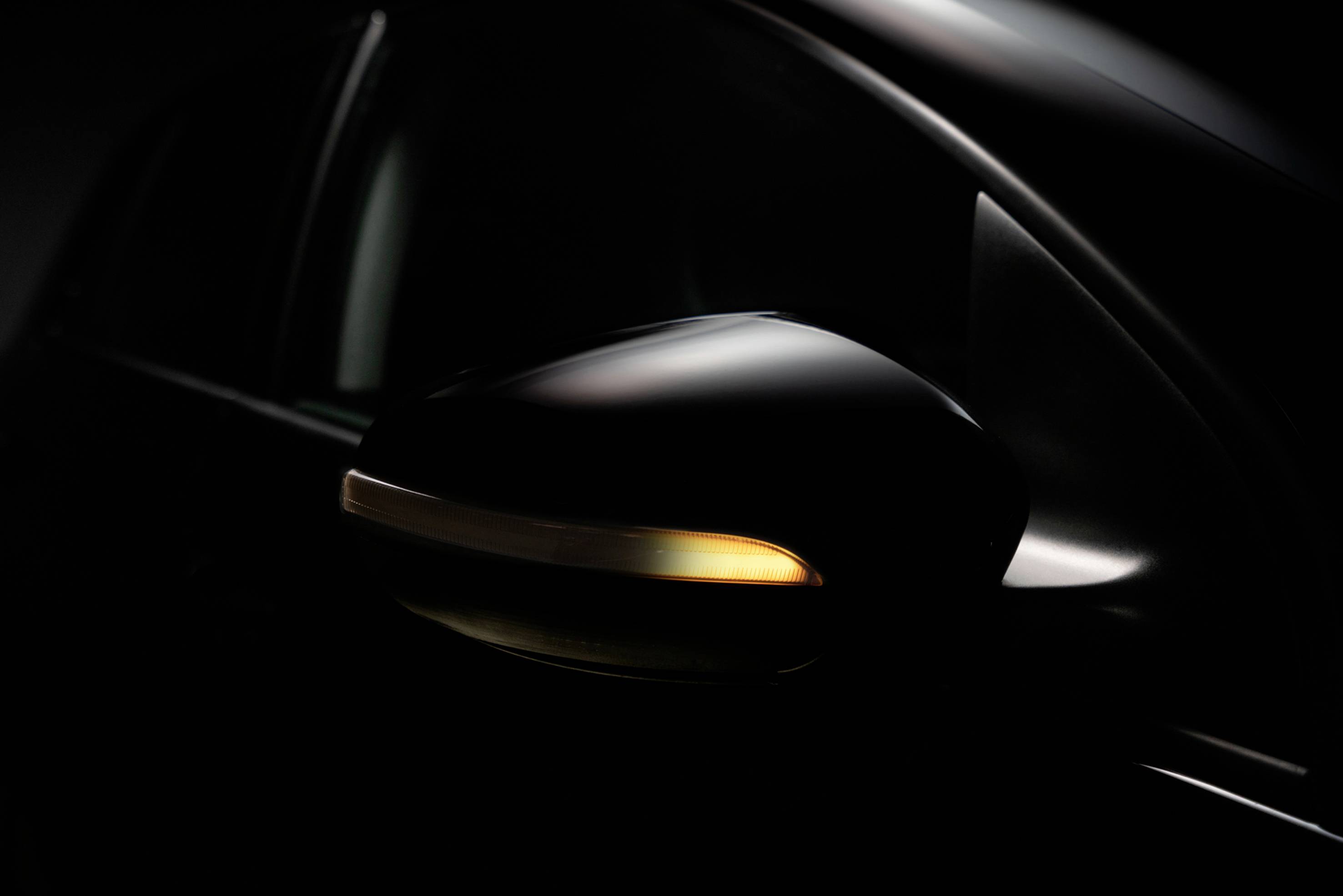 Nahaufnahme eines schwarzen Autospiegels mit leuchtendem Blinker im Dunkeln.