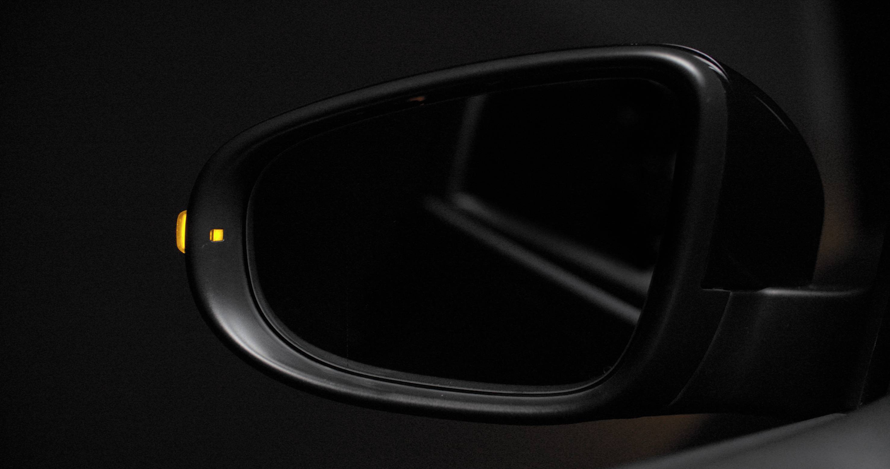 Rückspiegel eines Autos mit aktiviertem gelbem Warnlicht, das auf ein nahes Fahrzeug in der toten Winkelzone hinweist.