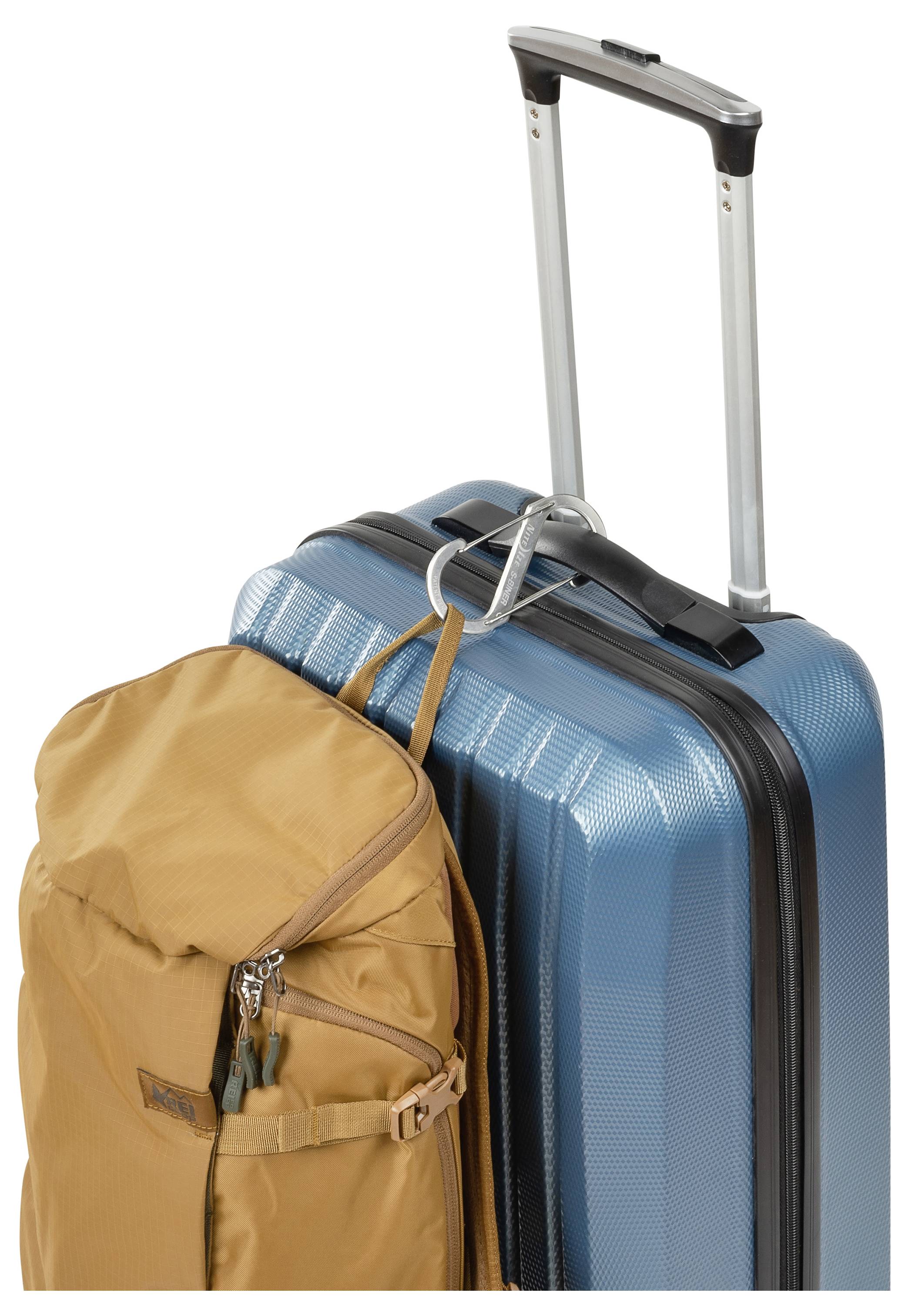 Ein blauer Hartschalenkoffer mit ausziehbarem Griff steht neben einem beigen Rucksack mit Reißverschlussfächern, was auf Reisen hindeutet.