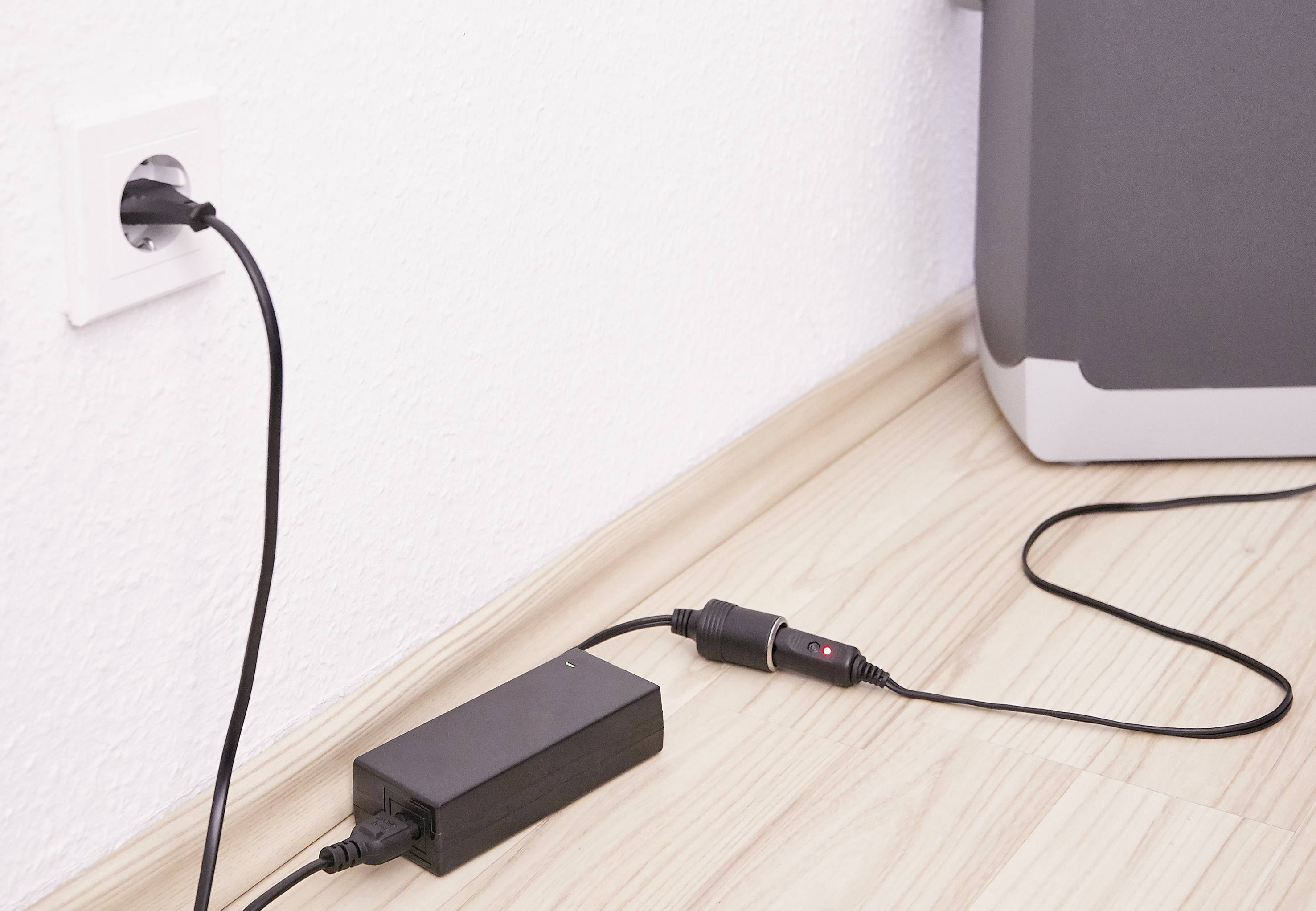 'Ein schwarzes Ladegerät ist mit einer Steckdose verbunden. Ein weiteres Kabel ist angeschlossen und geht zu einem elektronischen Gerät.'