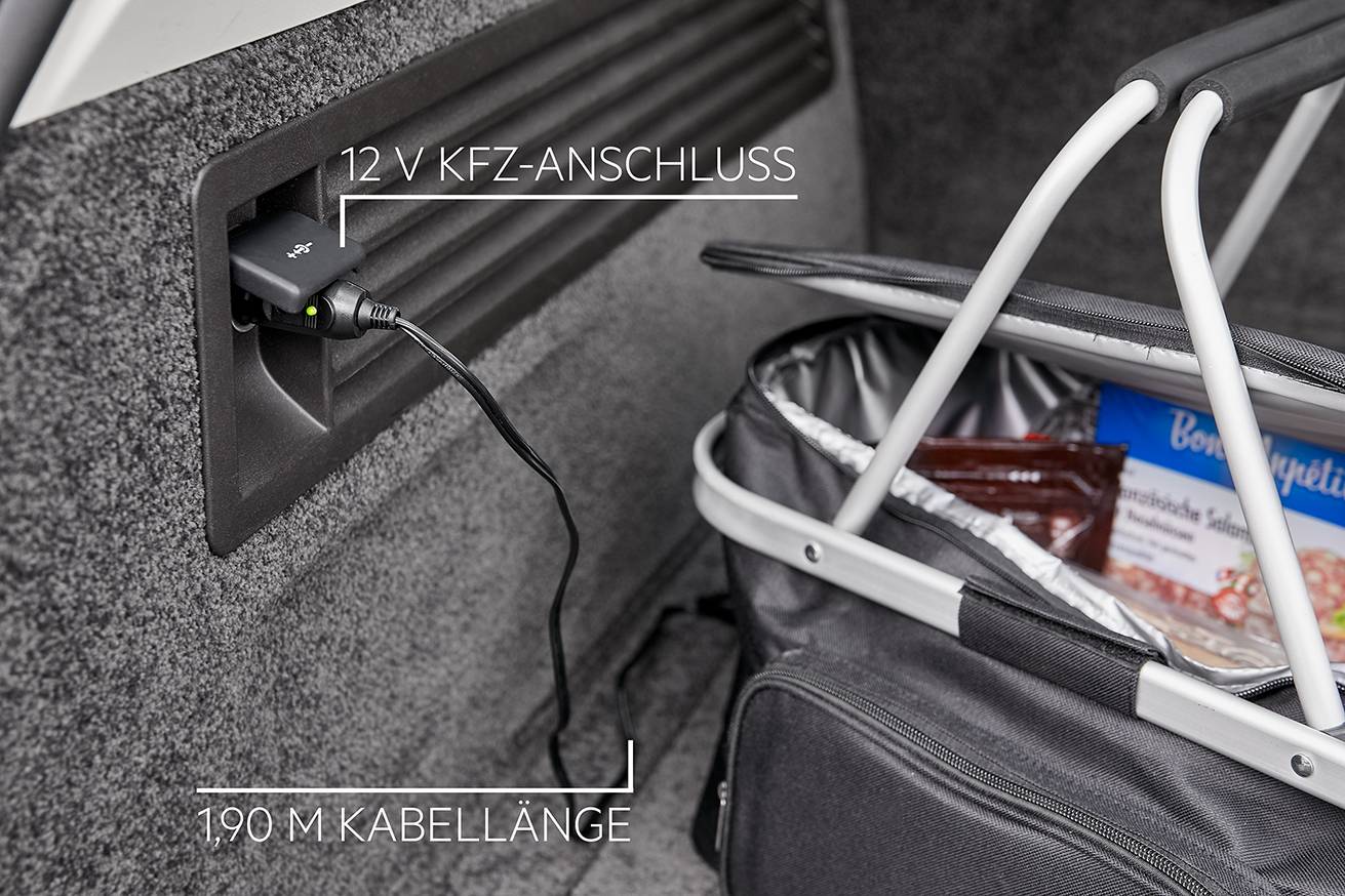 Ein Auto-Innenraum mit einem 12-V-KFZ-Anschluss, an dem ein Kabel angeschlossen ist. Daneben steht ein Einkaufskorb mit Lebensmitteln.