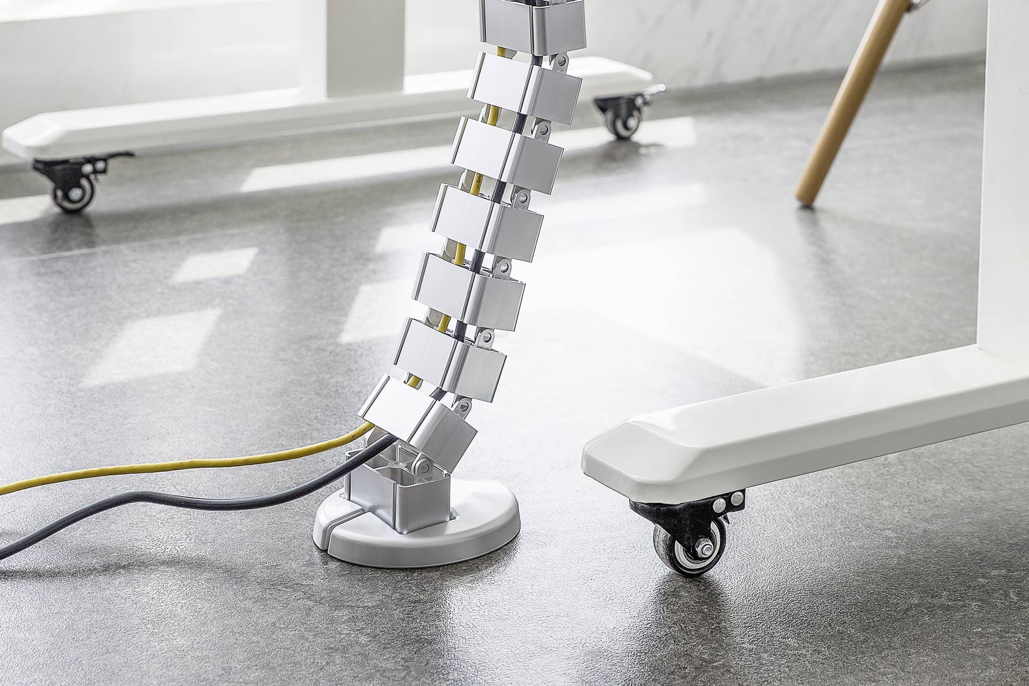 Ein Schreibtischkabelkanal in Form eines ummantelten Schlangenmotivs verbindet den Boden mit einem höhenverstellbaren Tisch.