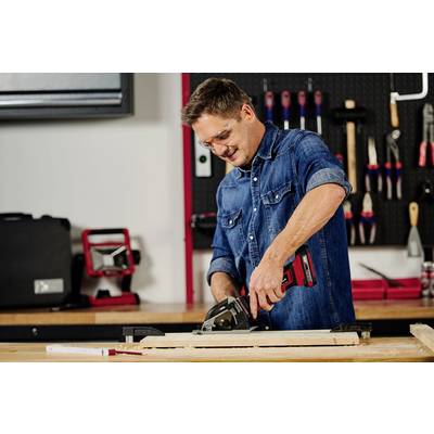 Mann in einer Werkstatt, der ein Holzbrett mit einer Kreissäge schneidet. Im Hintergrund sind Werkzeuge und Maschinen zu sehen.
