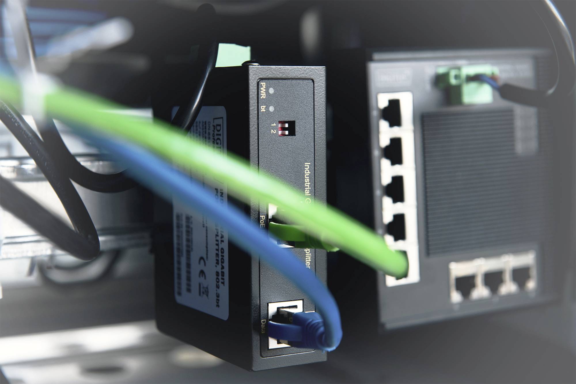 Netzwerkgeräte in einem Schrank mit mehreren angeschlossenen Kabeln, darunter ein grünes und ein blaues Kabel, verbunden mit Ports.