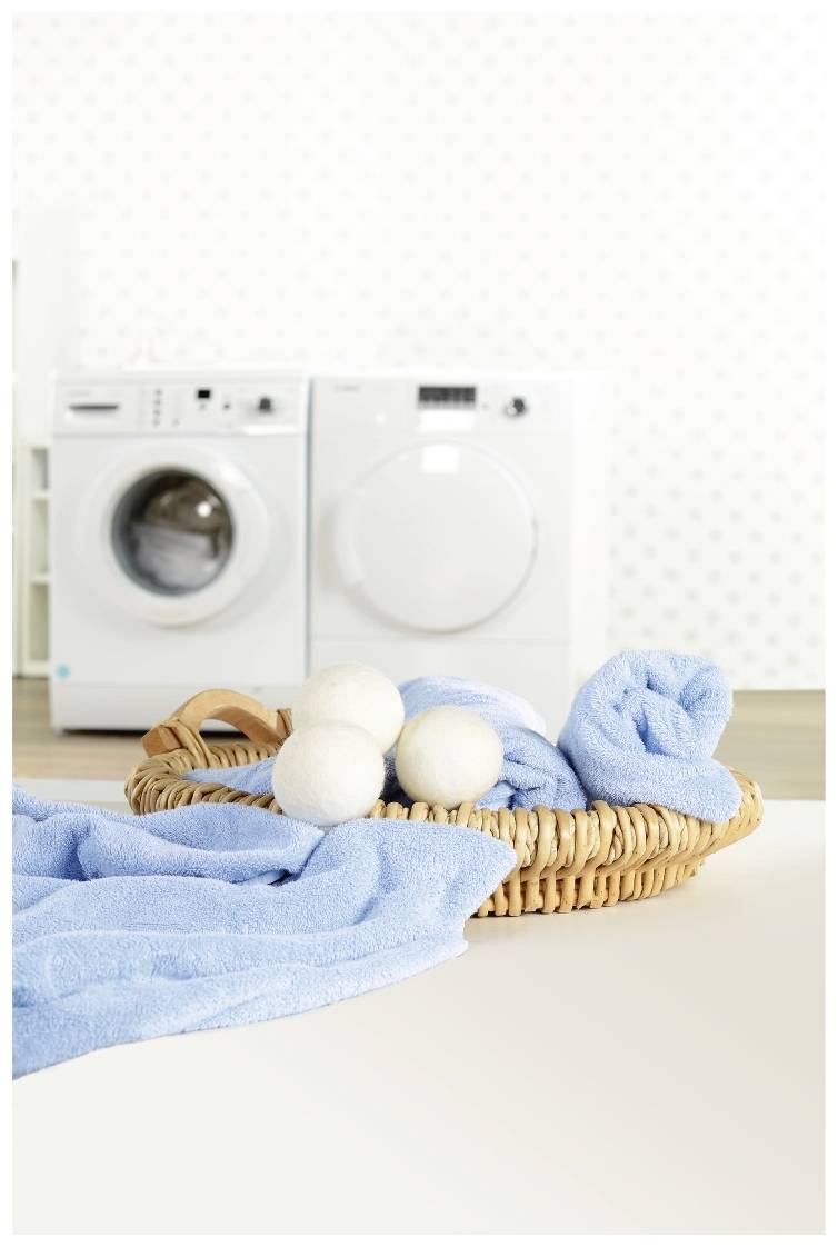 Ein Wäschekorb mit blauen Handtüchern und weißen Trocknerbällen steht vor einer Waschmaschine und einem Wäschetrockner.
