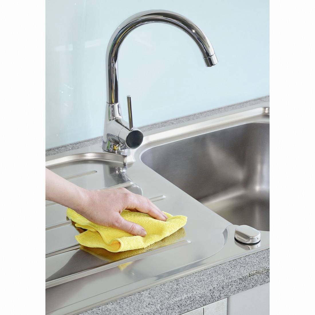 Eine Hand wischt mit einem gelben Tuch eine Spüle ab. Der Wasserhahn ist aus Edelstahl, und die Umgebung wirkt sauber und gepflegt.