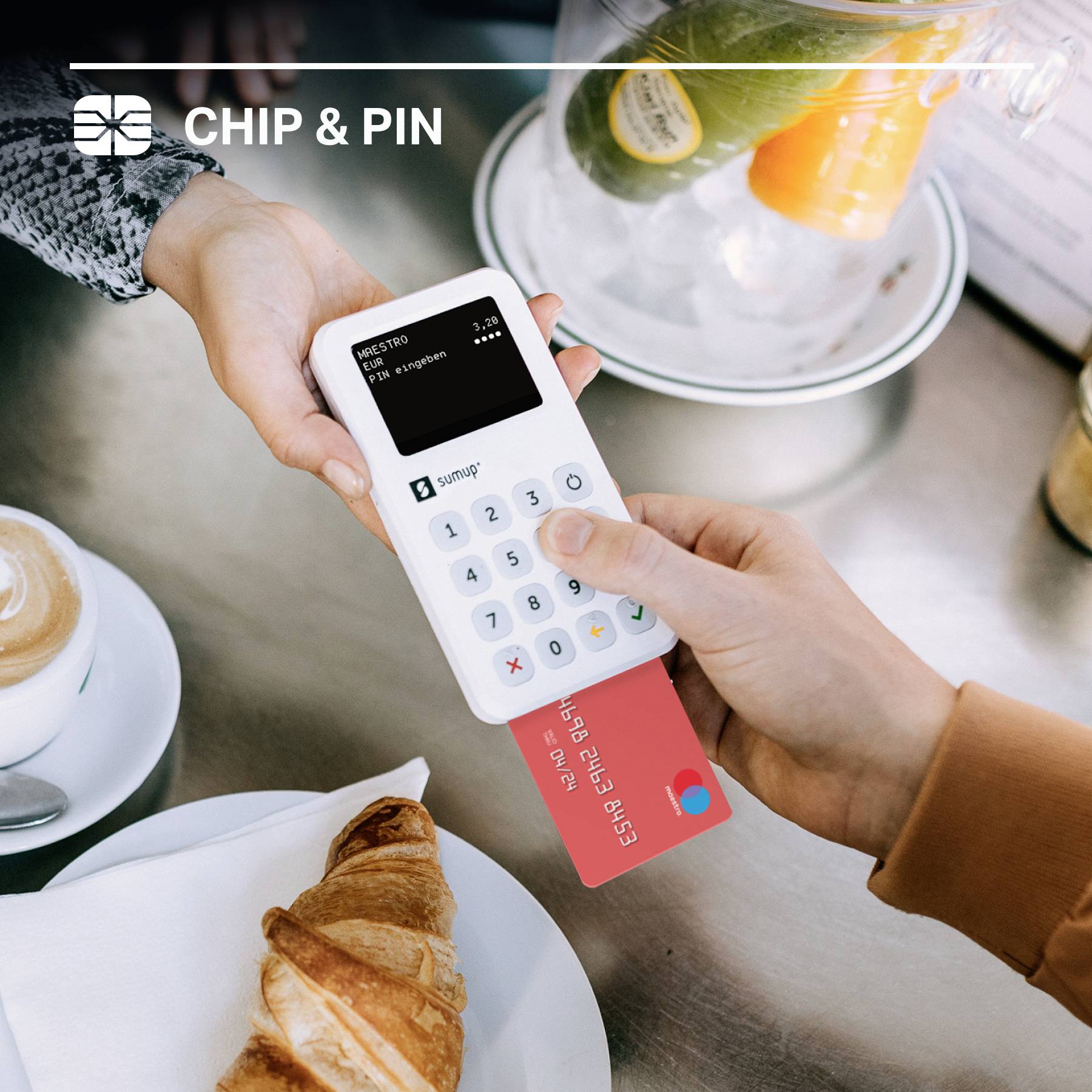 Person bezahlt mit einer Kreditkarte über ein mobiles Lesegerät in einem Café. Im Hintergrund sind eine Kaffeetasse und ein Croissant zu sehen.