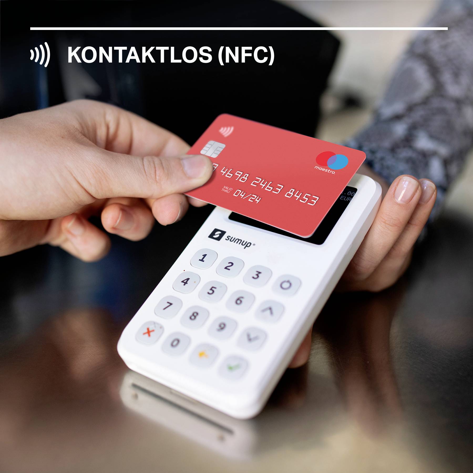 Person hält eine rote Kreditkarte über ein weißes Kartenlesegerät zur kontaktlosen Zahlung; auf dem Gerät erscheint 'Kontaktlos (NFC)'.