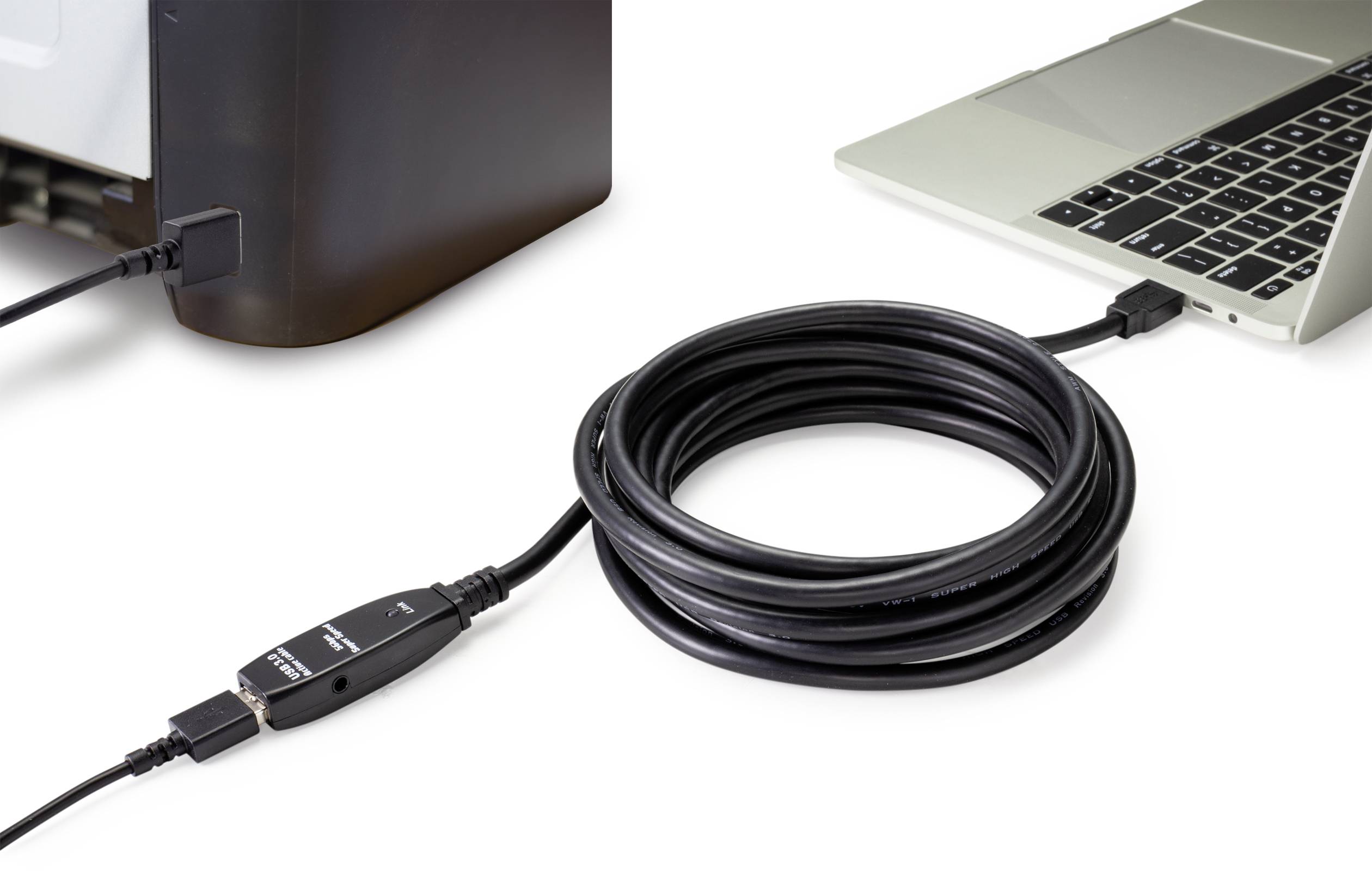 Ein schwarzes USB-Kabel verbindet einen Laptop mit einem Drucker. Das Kabel ist aufgewickelt und liegt zwischen den Geräten auf einem Tisch.