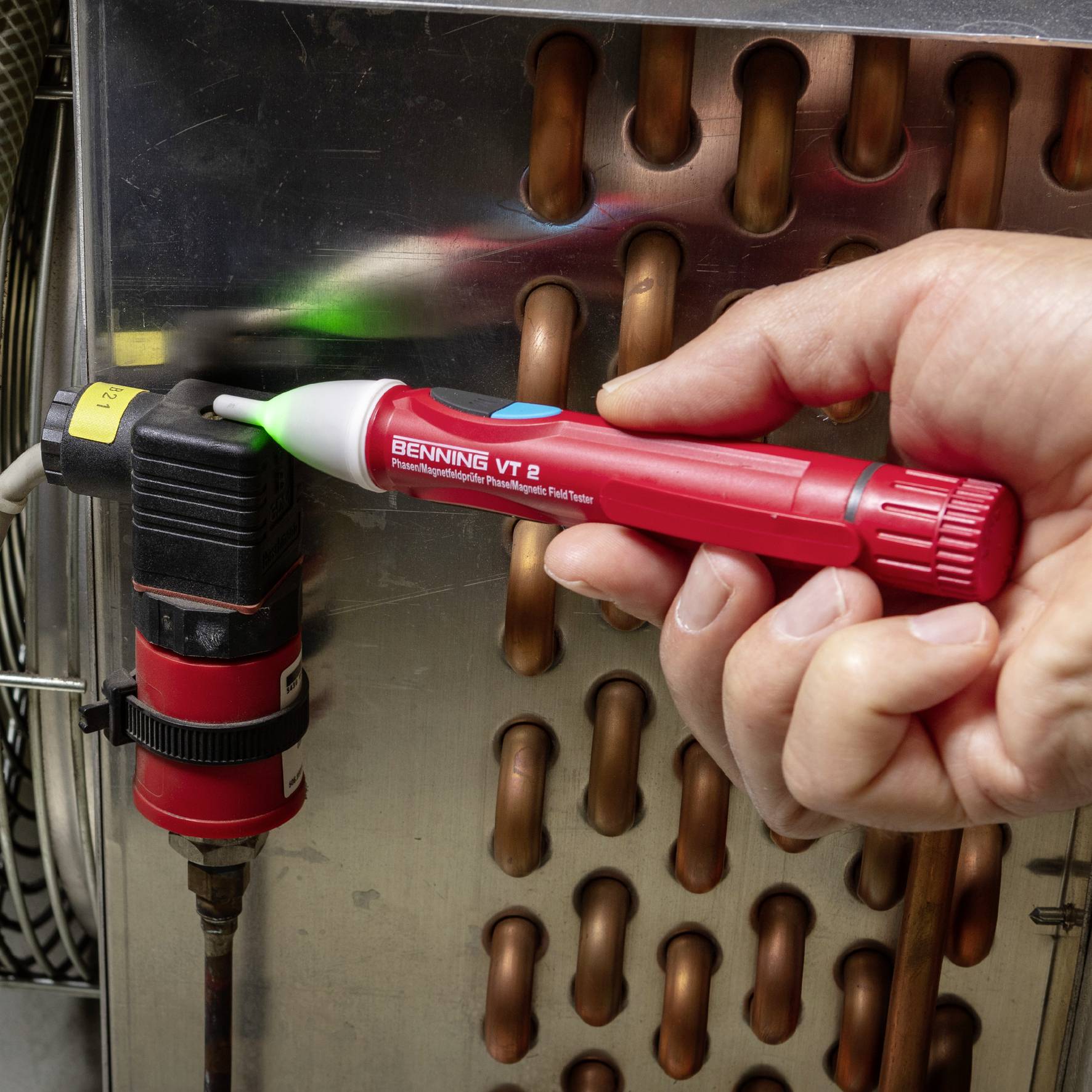 Eine Hand hält einen Berührungslosen Spannungsprüfer an ein elektrisches Bauteil, um Spannung an einem Kupferrohr zu überprüfen.