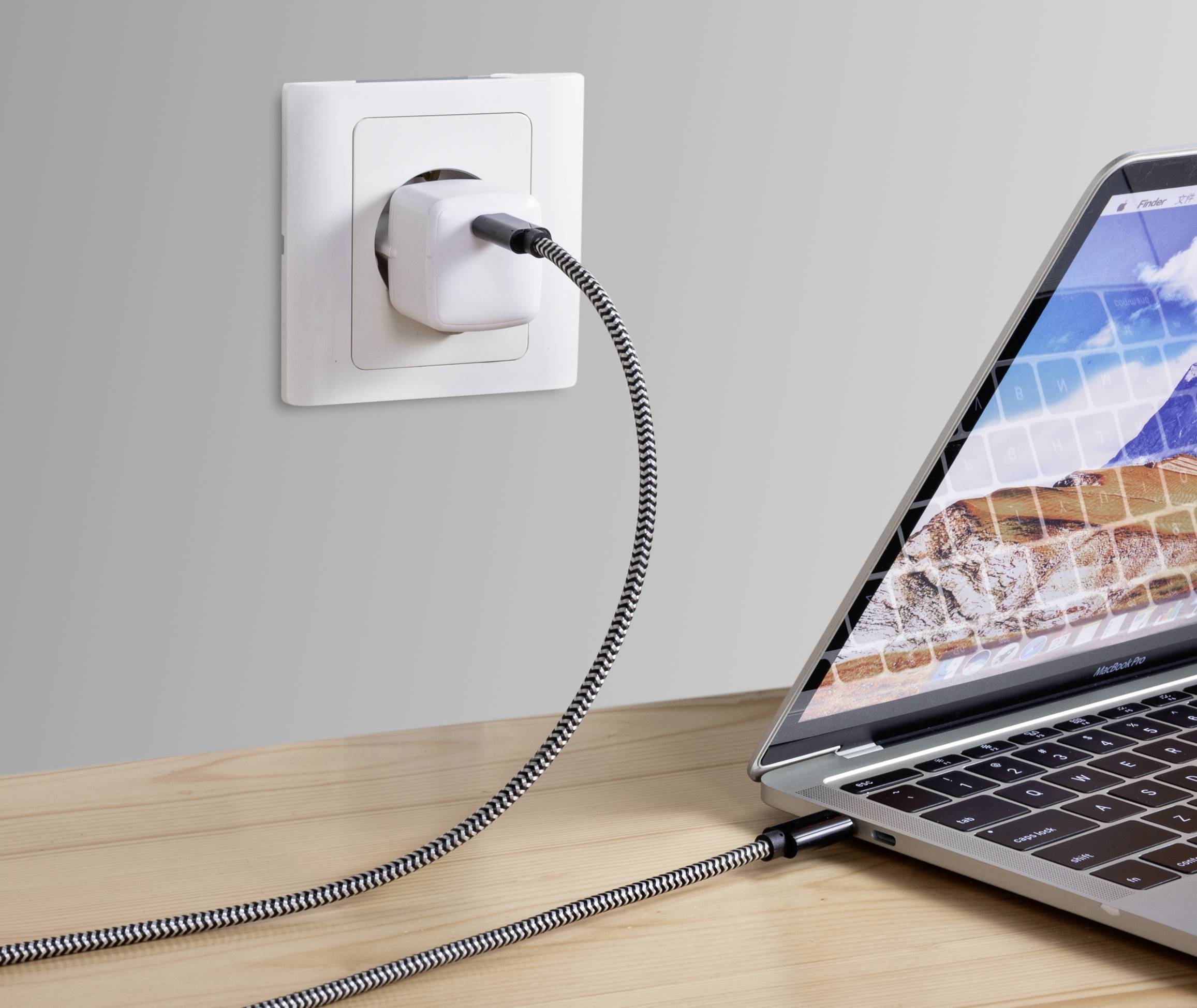 Ein Laptop wird mit einem Stromkabel an eine Steckdose angeschlossen. Das Kabel hat ein geflochtenes Muster.