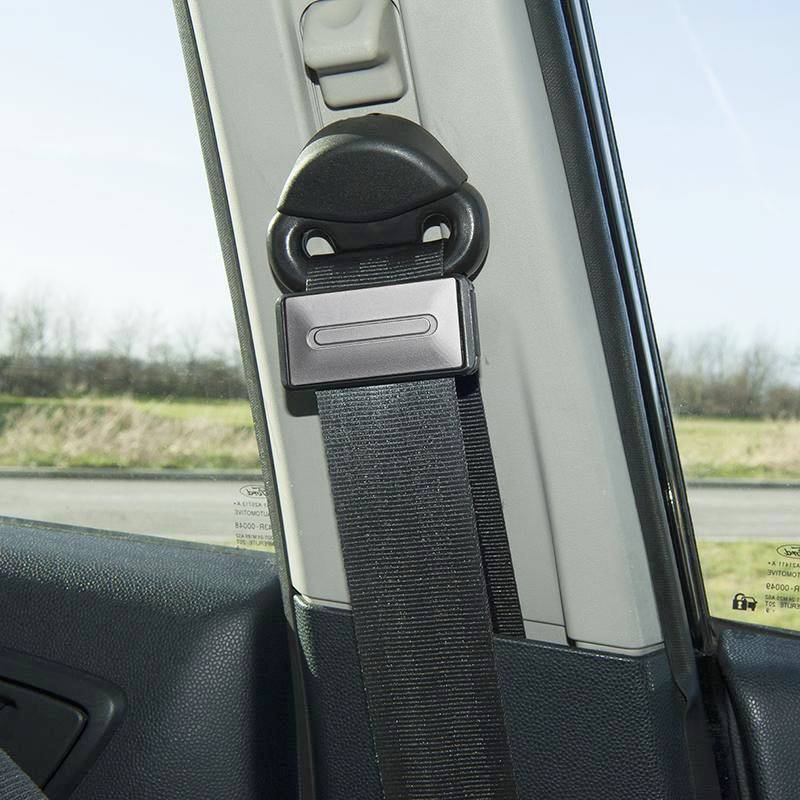 Ein Sicherheitsgurt ist an seiner Halterung in einem Auto befestigt, bereit für den Gebrauch. Im Hintergrund ist eine Straße zu sehen.