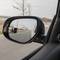 Ein Auto-Außenspiegel zeigt die Sicht nach hinten auf eine leere Landstraße an einem Wintertag, mit kahlen Bäumen am Straßenrand.
