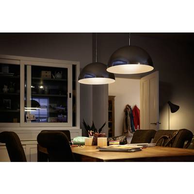 Zwei große, leuchtende Deckenlampen über einem Tisch mit Stühlen in einem gemütlich beleuchteten Raum, mit Schreibmaterialien auf dem Tisch.