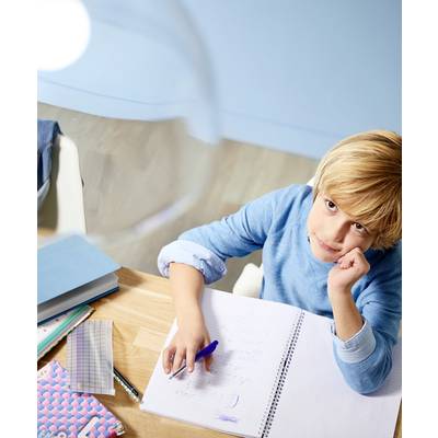Ein Kind in blauem Pullover schaut nachdenklich beim Schreiben in ein Notizbuch. Auf dem Tisch liegen Notizblöcke und Lernmaterial.