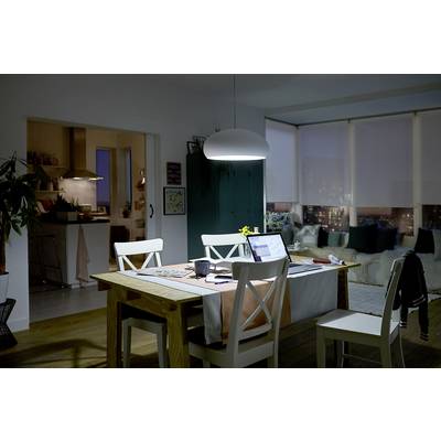 Ein Wohnzimmer bei Nacht mit einem Tisch im Vordergrund. Auf dem Tisch sind ein Laptop, ein Notizbuch und eine Kaffeetasse. Im Hintergrund eine Küche.