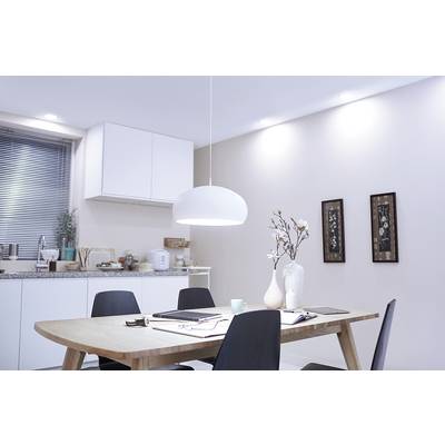 Wohnzimmer mit Esstisch, umgeben von vier schwarzen Stühlen. Weiße Küchenschränke und Dekorationen im Hintergrund, helle Wandbeleuchtung.