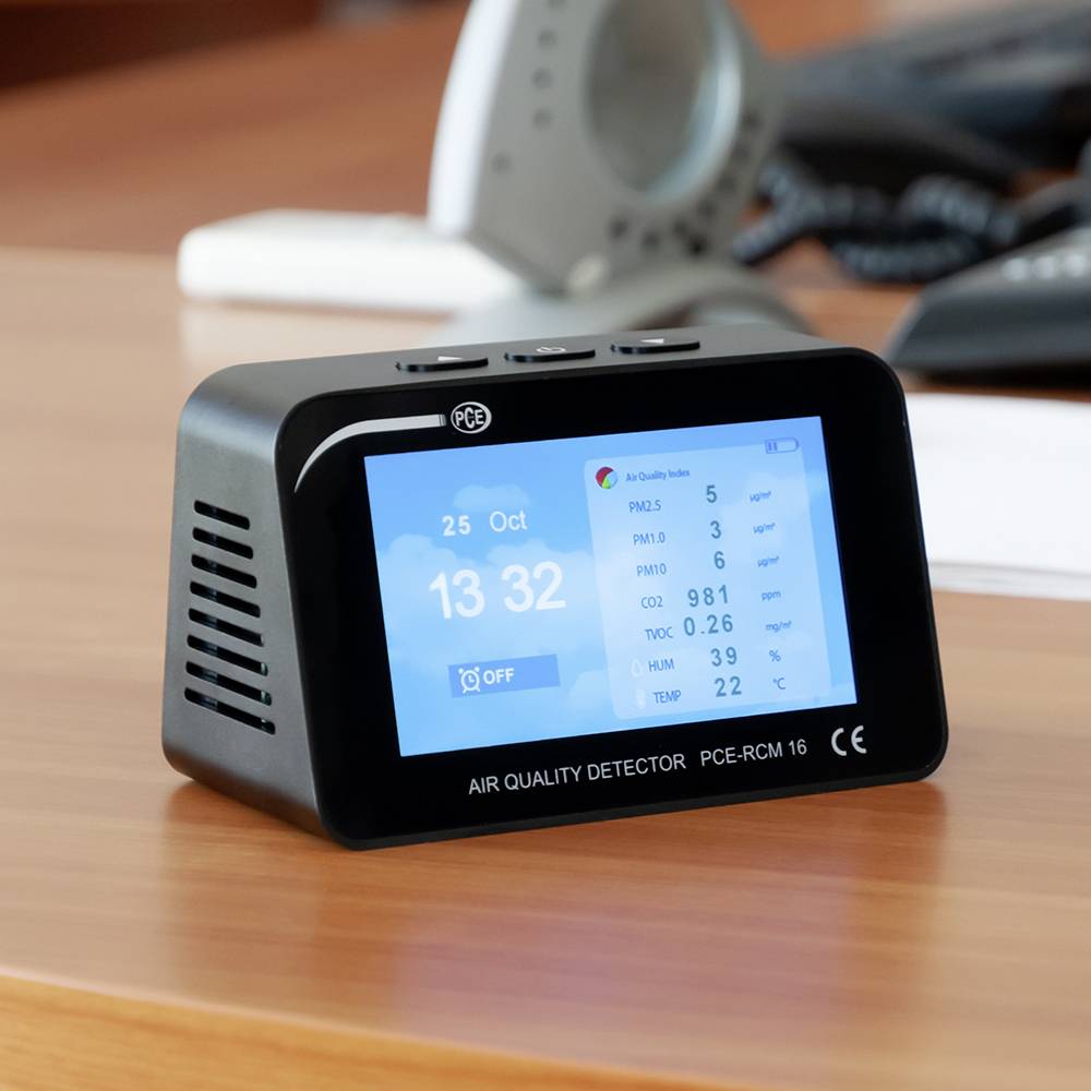 Ein Luftqualitätsmessgerät auf einem Tisch zeigt verschiedene Messwerte, darunter PM10, PM2.5, Temperatur und Luftfeuchtigkeit an.