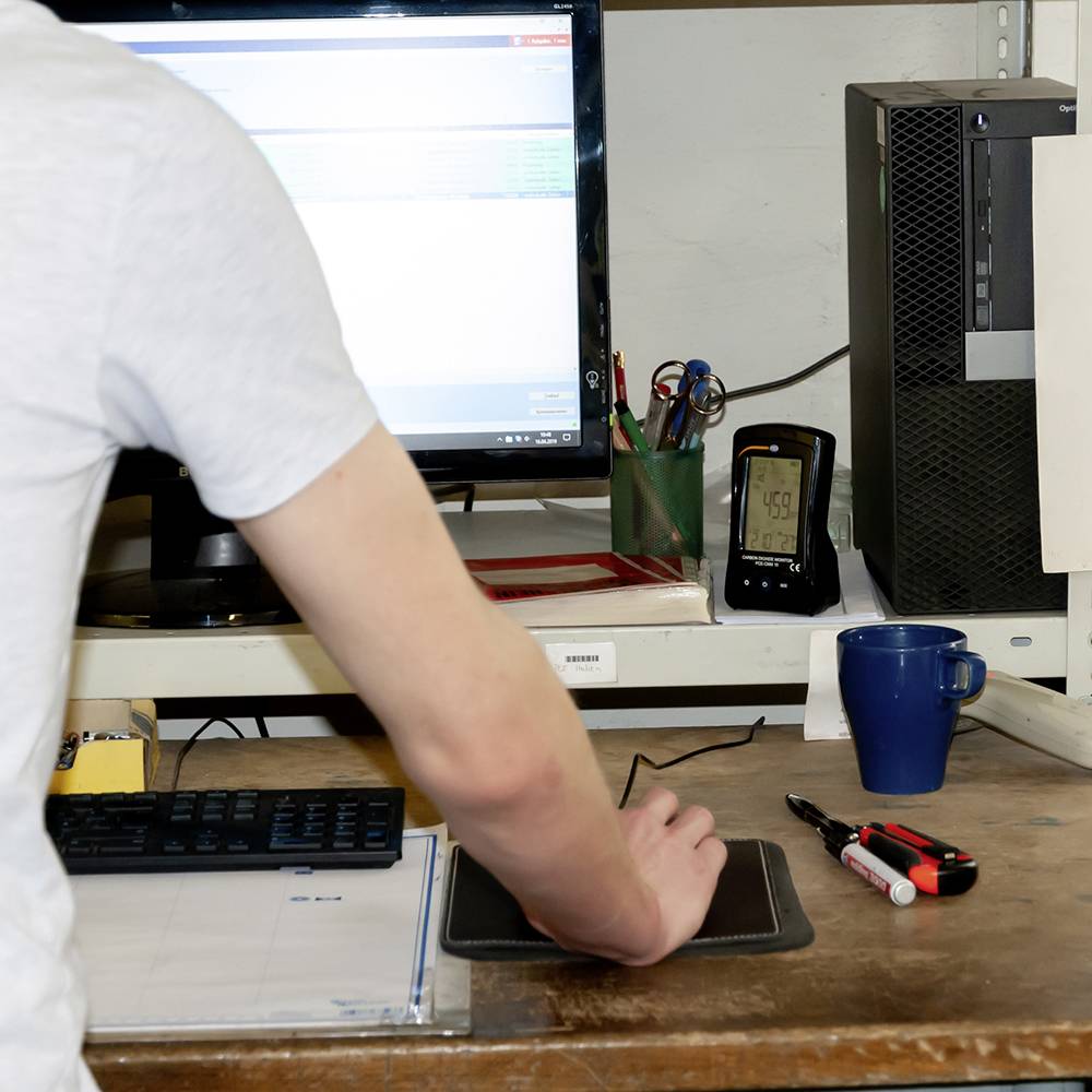 Ein Mann arbeitet an einem Schreibtisch mit einem Computerbildschirm, einer Tastatur und verschiedenen Büromaterialien.