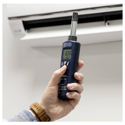Hand hält ein digitales Thermometer in der Nähe einer Klimaanlage-Lüftung und misst die Innentemperatur.