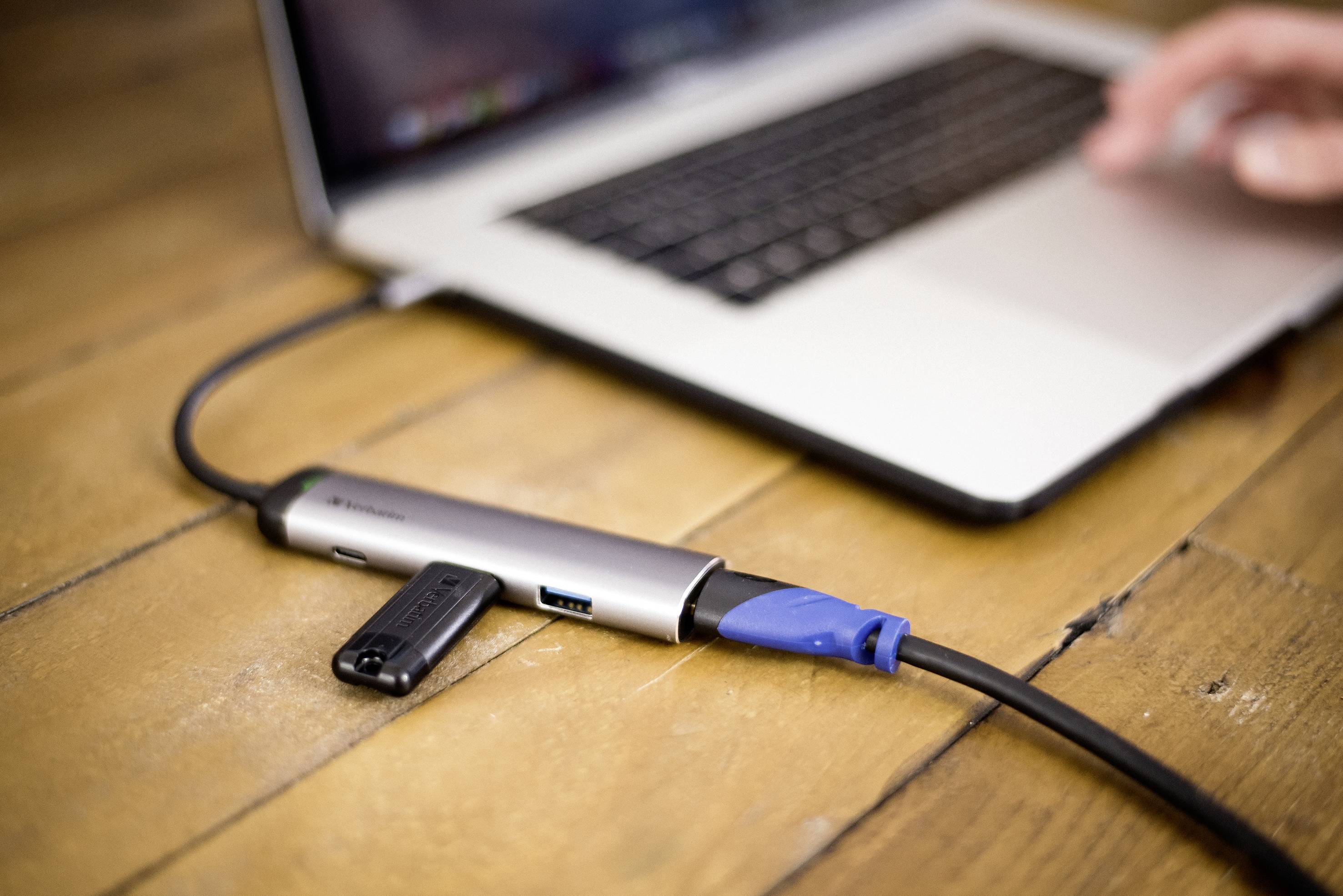 Ein Laptop mit einer Hand auf der Tastatur ist über einen USB-Hub mit einem Netzwerkkabel und einem USB-Stick verbunden.
